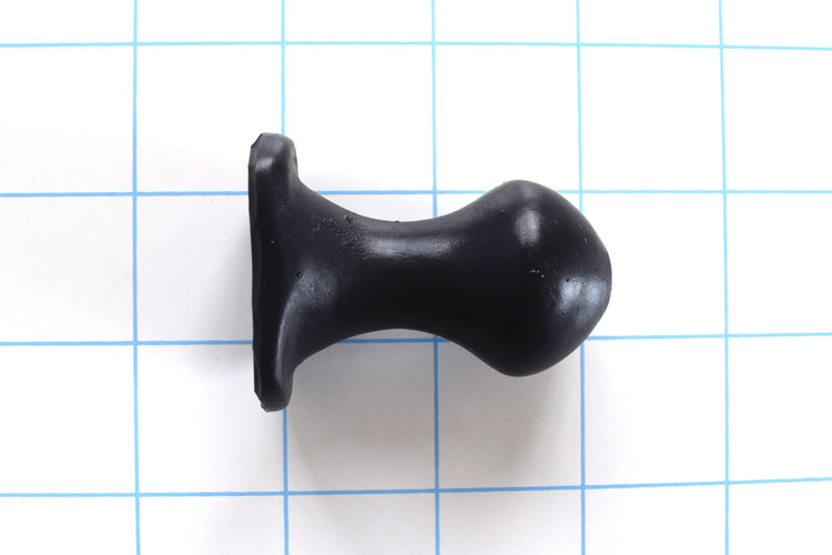 Nubby OF short black silicone retention plug with a bulbous tip and an oval safety flange on a blue grid background