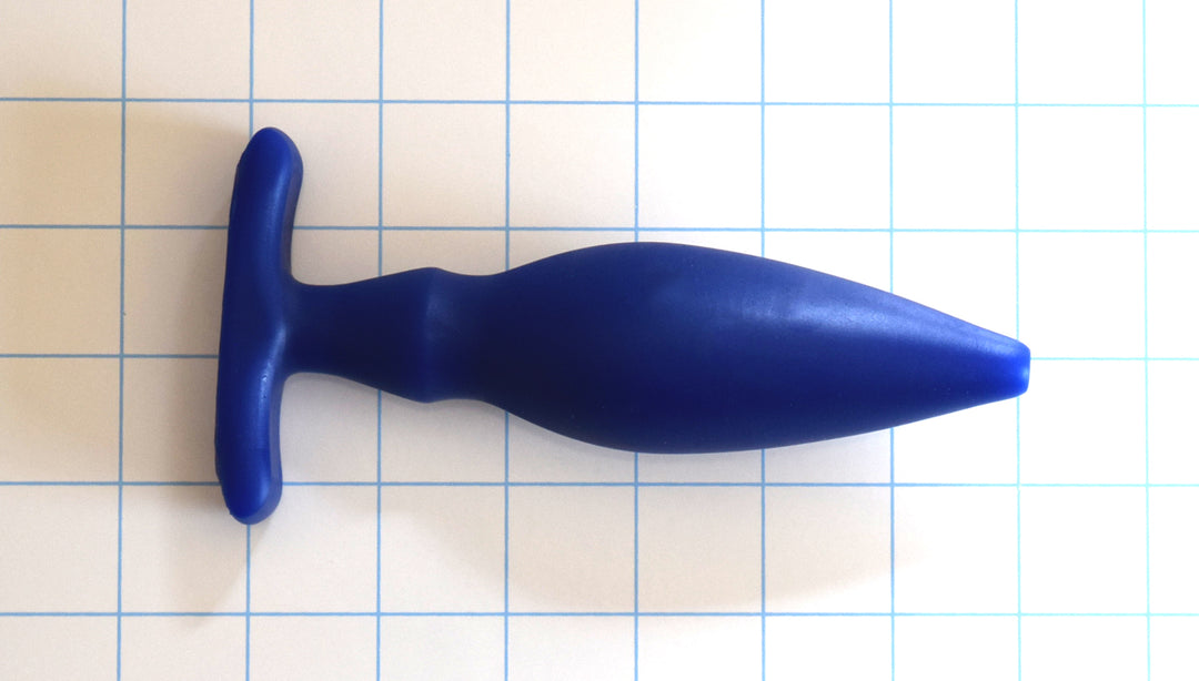 OF 1.6 blue silicone enema nozzle on a white with blue grid background, showcasing its 0.5-inch rounded tip, gradual 1.6-inch taper, dual-stage retention valleys, and a 3-inch wide contoured oval base flange