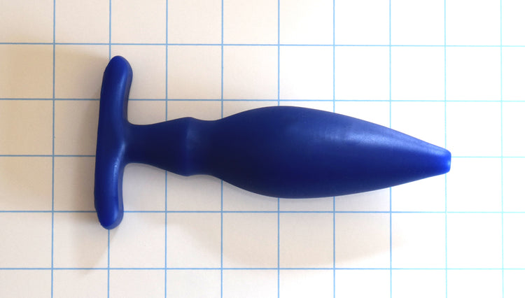 OF 1.6 blue silicone enema nozzle on a white with blue grid background, showcasing its 0.5-inch rounded tip, gradual 1.6-inch taper, dual-stage retention valleys, and a 3-inch wide contoured oval base flange