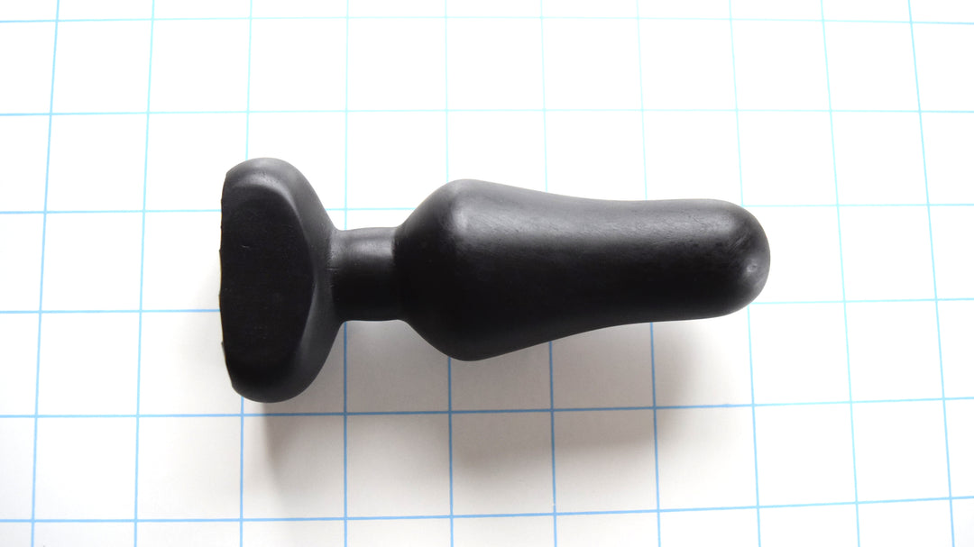 OF 1 black silicone enema nozzle resting horizontally on a blue grid background, displaying its 3.75-inch insertable length, 1.6-inch maximum bulbous swell, and contoured oval safety flange.