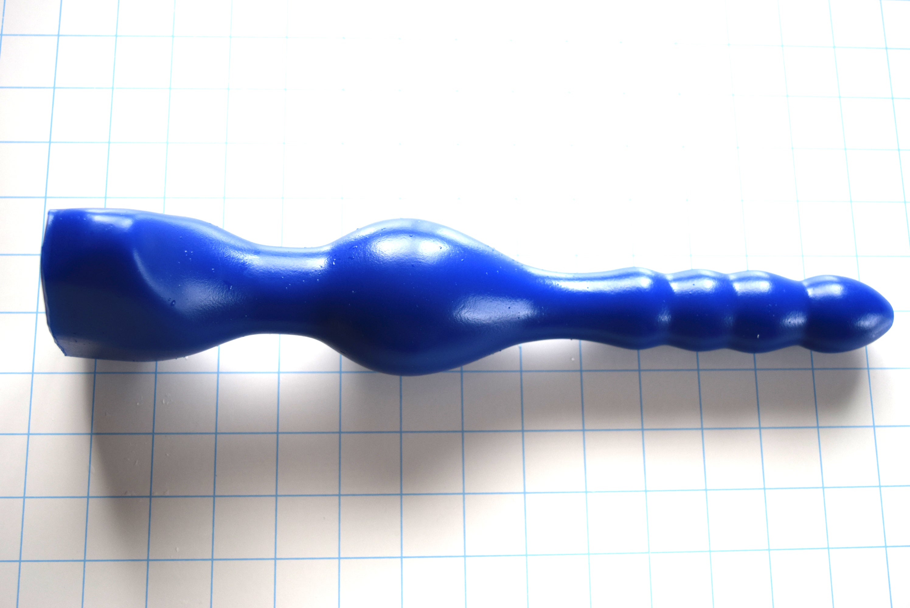 Blue OF 13 silicone enema nozzle featuring a multi-ribbed shaft, 2.5-inch retention ball, and gluteal flange resting on grid paper.