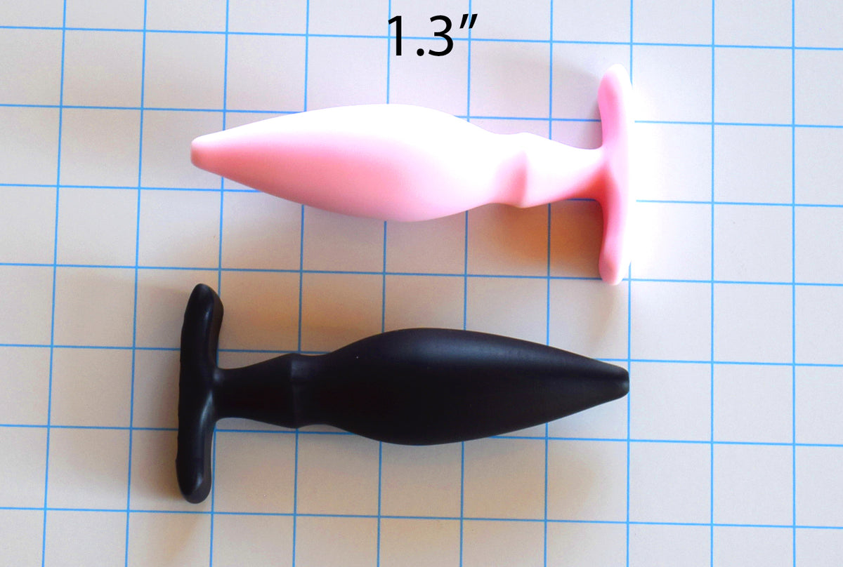 1.3-inch OF Wing silicone enema nozzle on a grid background showing the pink and black variants, curved body, retention valley, and winged base flange.