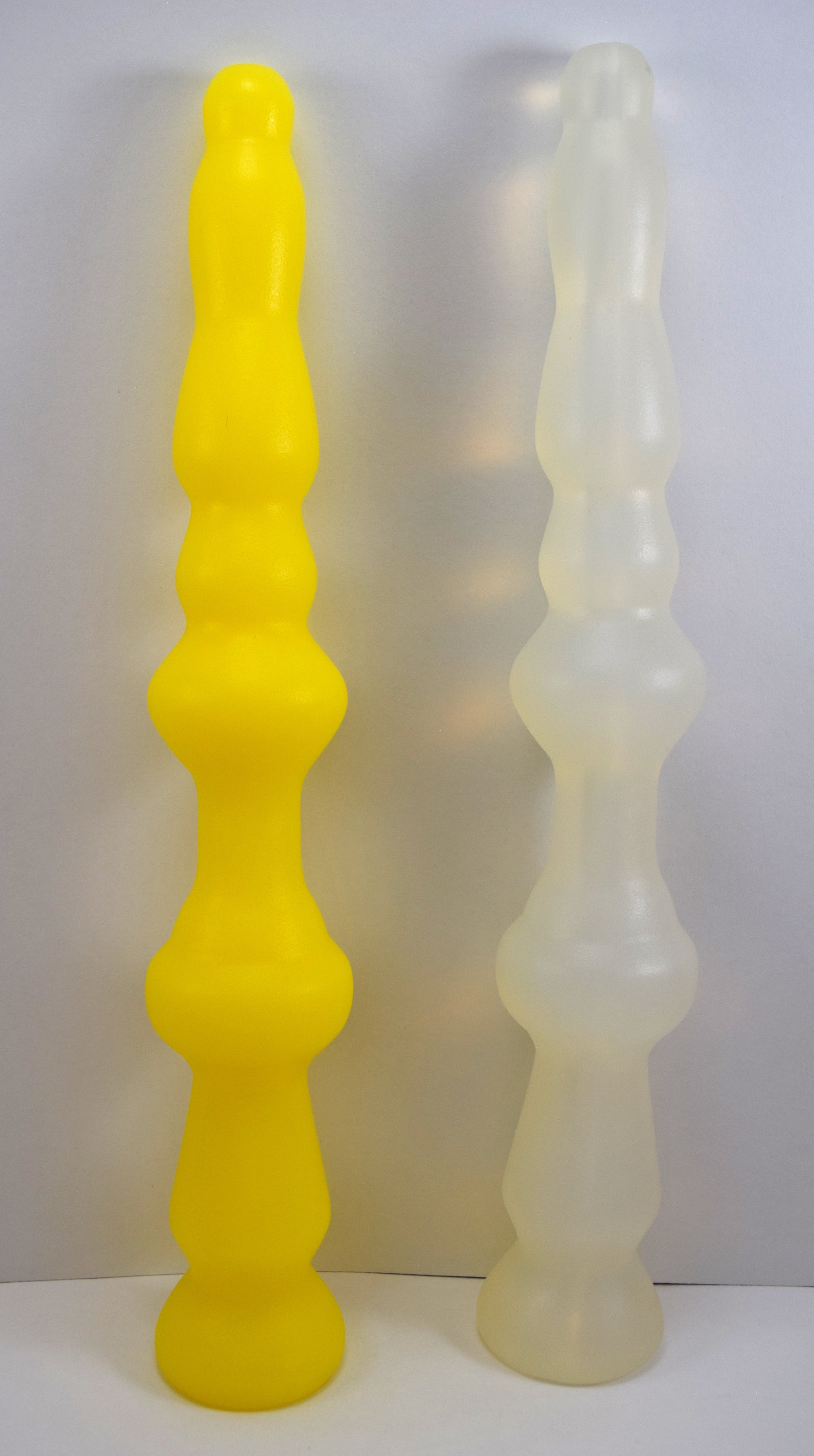 Yellow and translucent white PSP silicone enema nozzles standing side by side showcasing multi-stage graduated expansion bulbs and tapered base flanges.