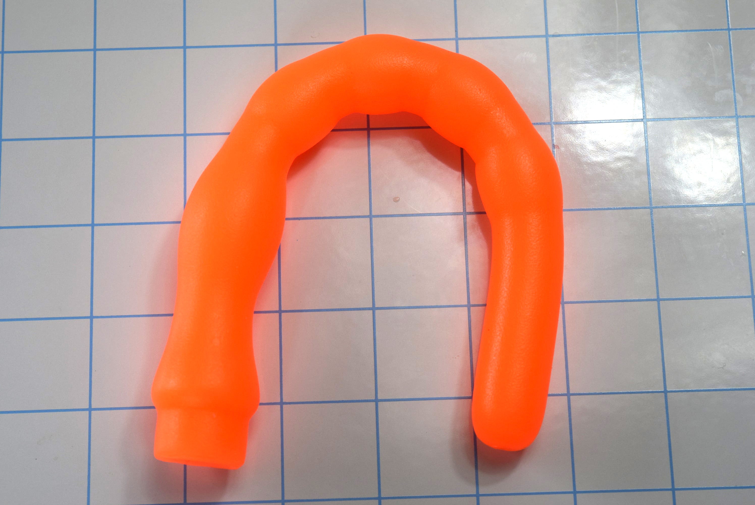 8 inch orange ribbed throat trainer bent in U-shape demonstrating soft flexible silicone firmness.