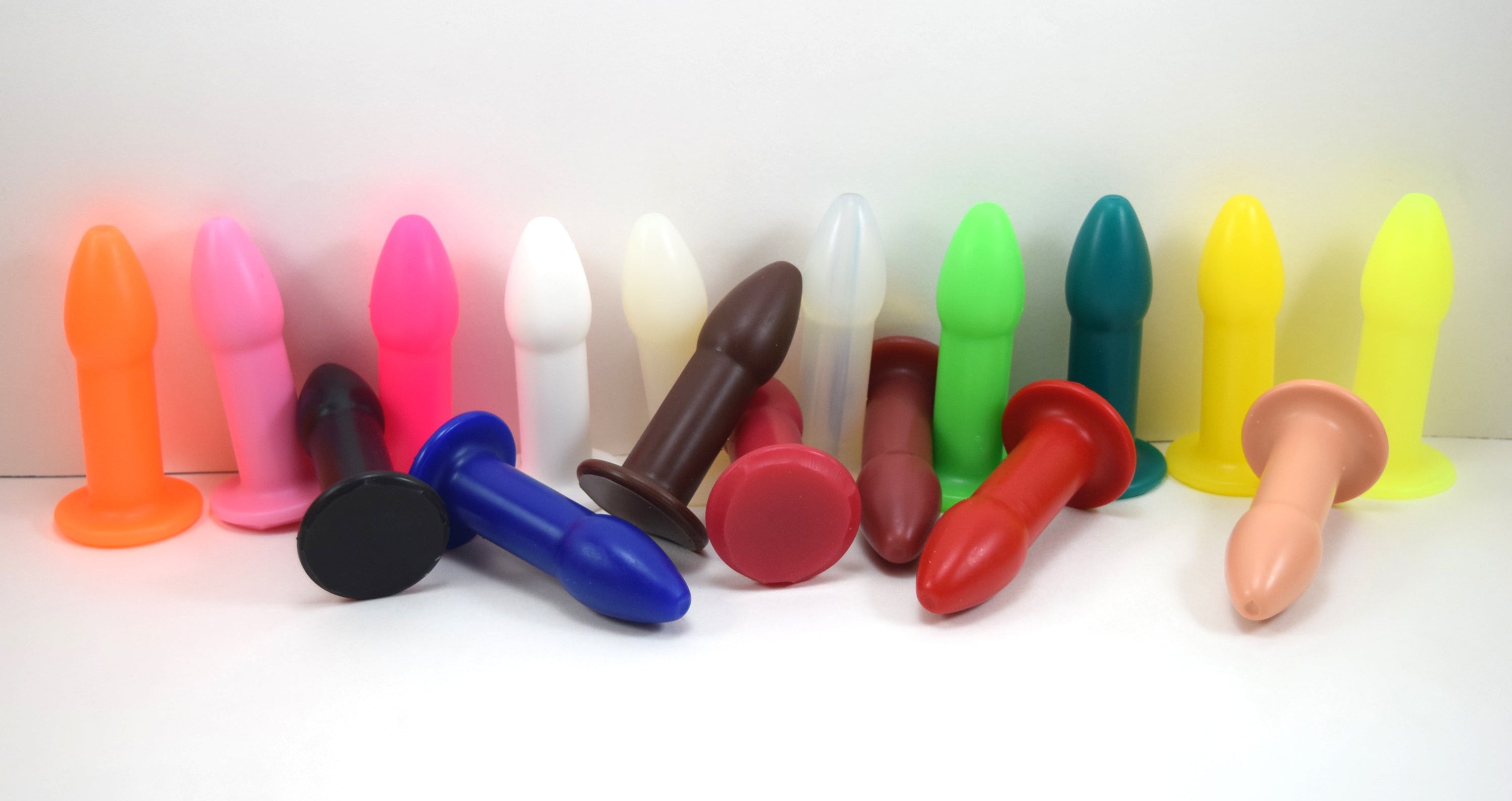 A collection of 1-inch silicone rectal training dilators in various colors standing and lying down on a white surface.