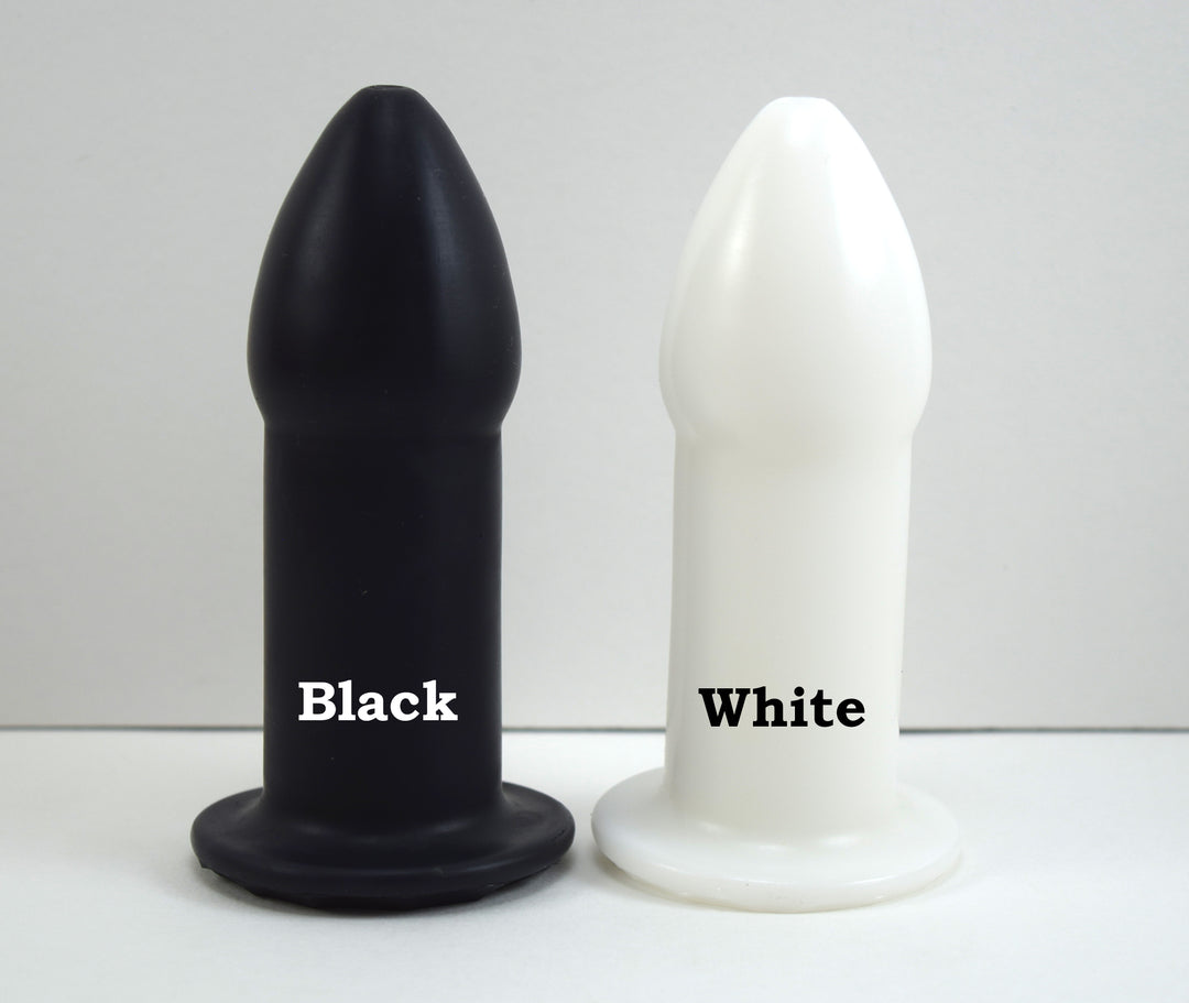 Black and white silicone rectal training dilators standing side-by-side on a white surface labeled with color names.
