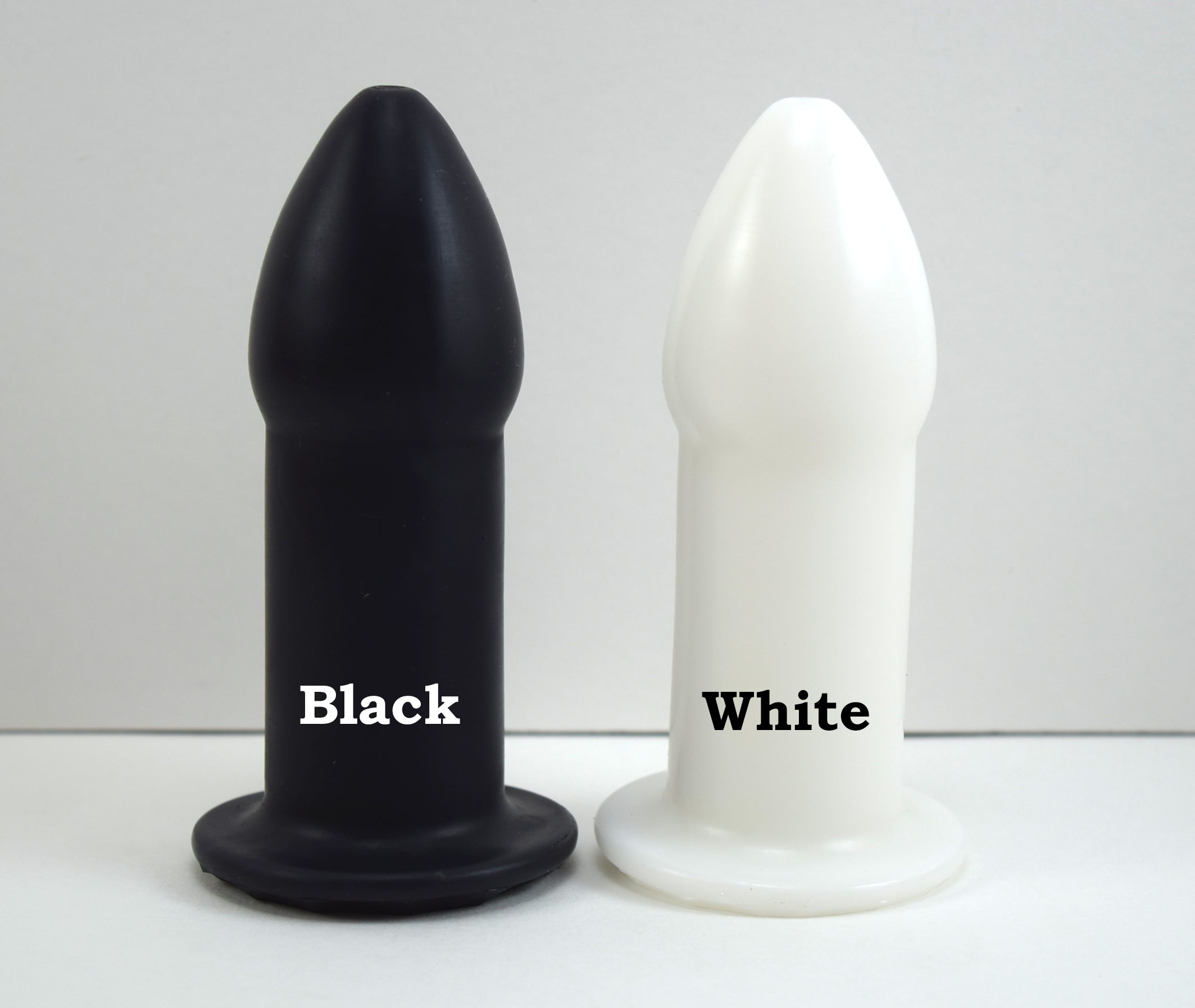 Black and white silicone rectal training dilators standing side-by-side on a white surface labeled with color names.