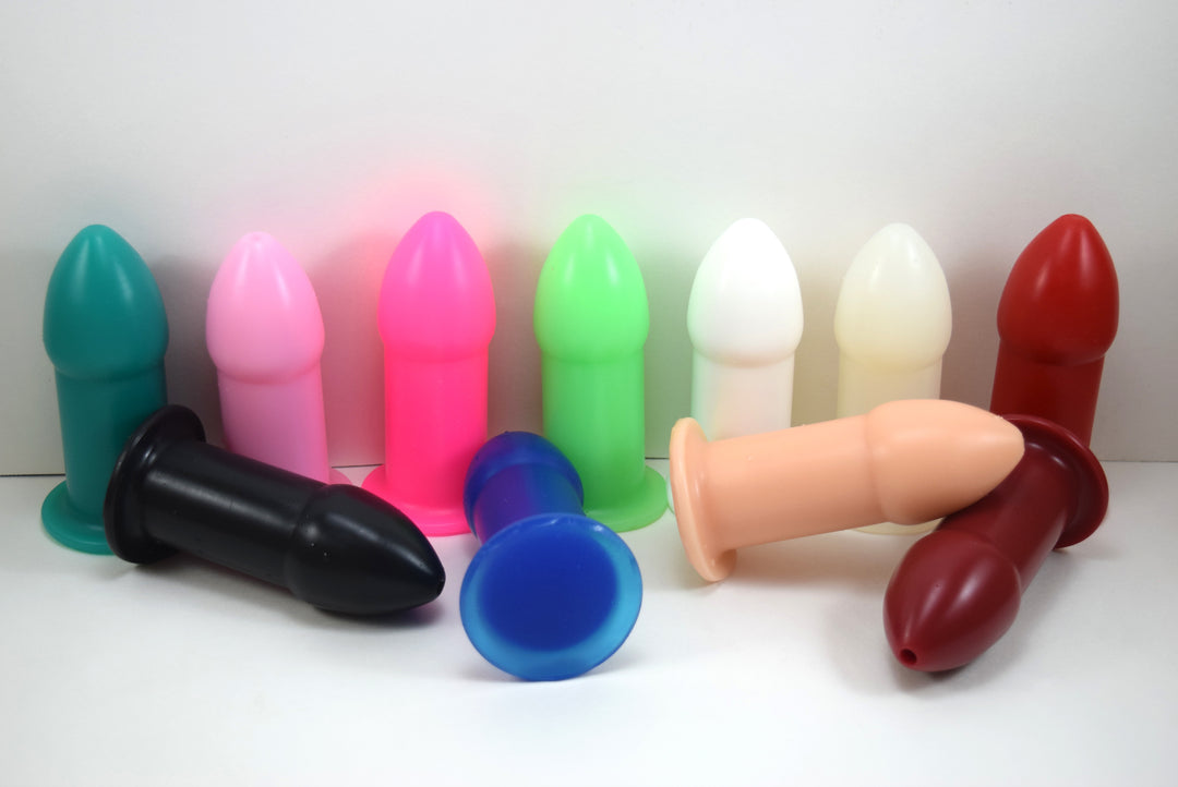 A multi-color assortment of 1.75-inch silicone rectal training dilators standing and lying down on a white surface.