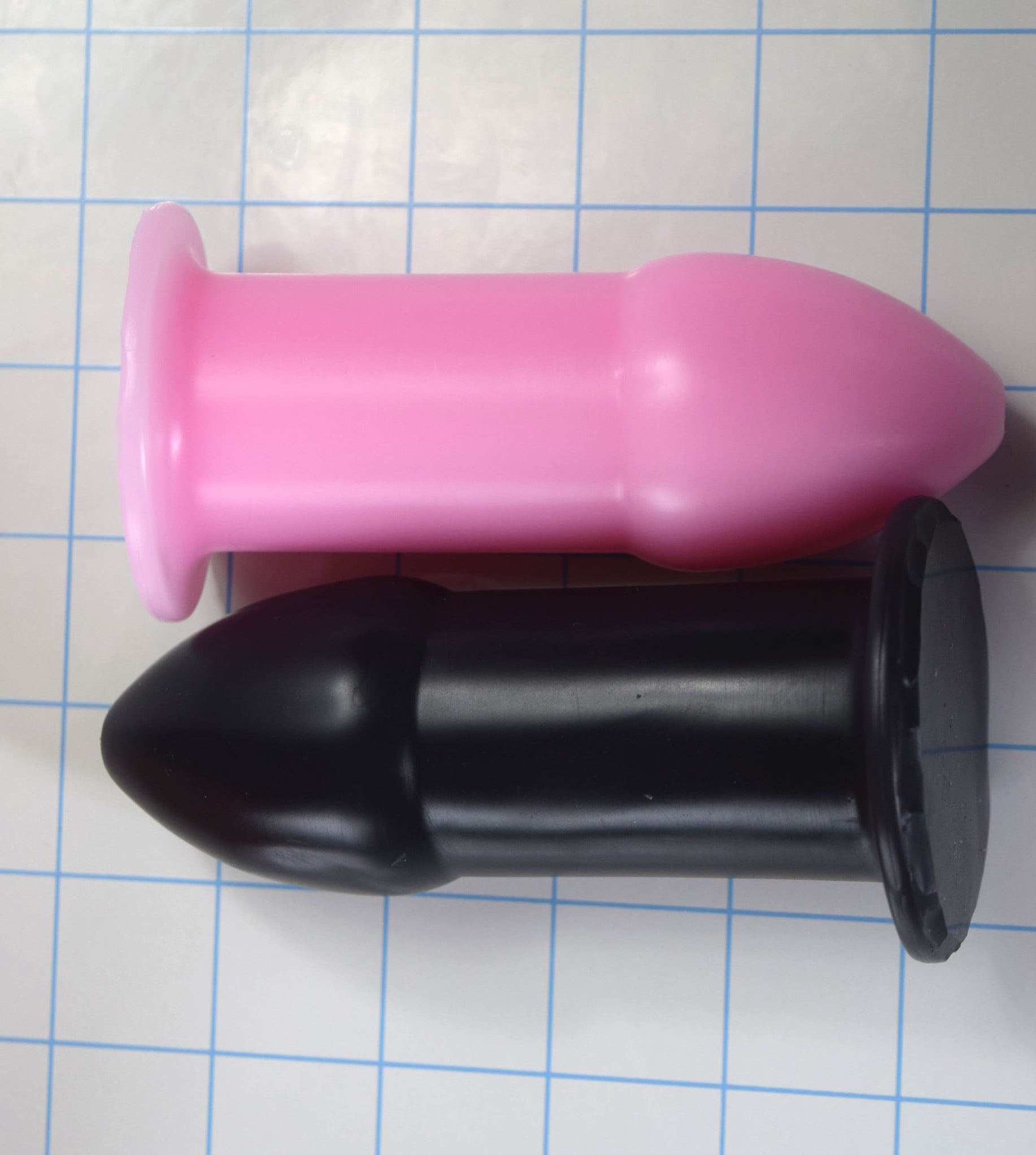Black and pink 1.75-inch silicone rectal training dilators viewed from above on a blue grid background.