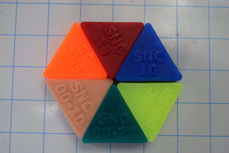 Overhead view of multi-colored sample firmness triangles showing different density levels and embossed softness numbers on a grid background.