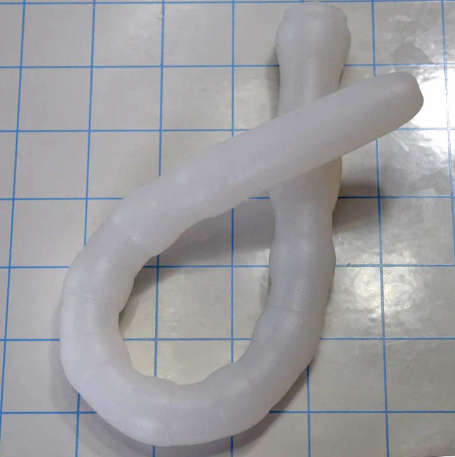 Coiled translucent white Shower Shooter 13-inch silicone enema nozzle on measurement grid demonstrating flexibility.