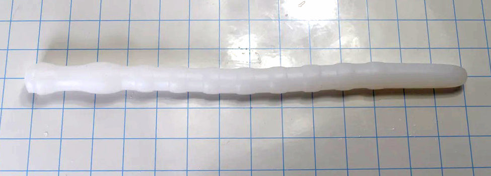 Shower Shooter 13-inch silicone enema nozzle laid flat on grid paper showing 8 expansion ribs, smooth entry tip, and retention neck.