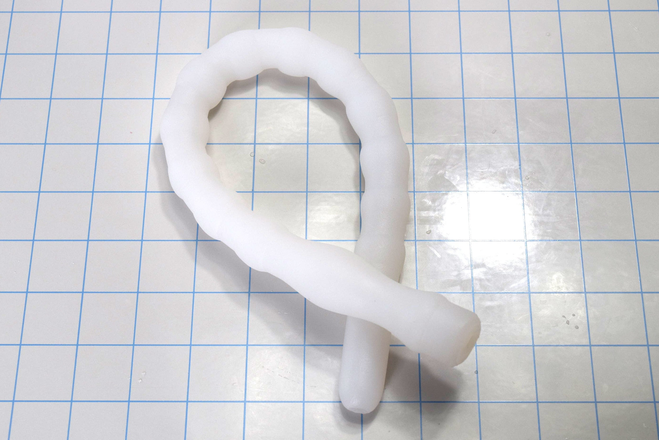 Coiled translucent white Shower Shooter 18-inch silicone enema nozzle on measurement grid displaying extreme flexibility.