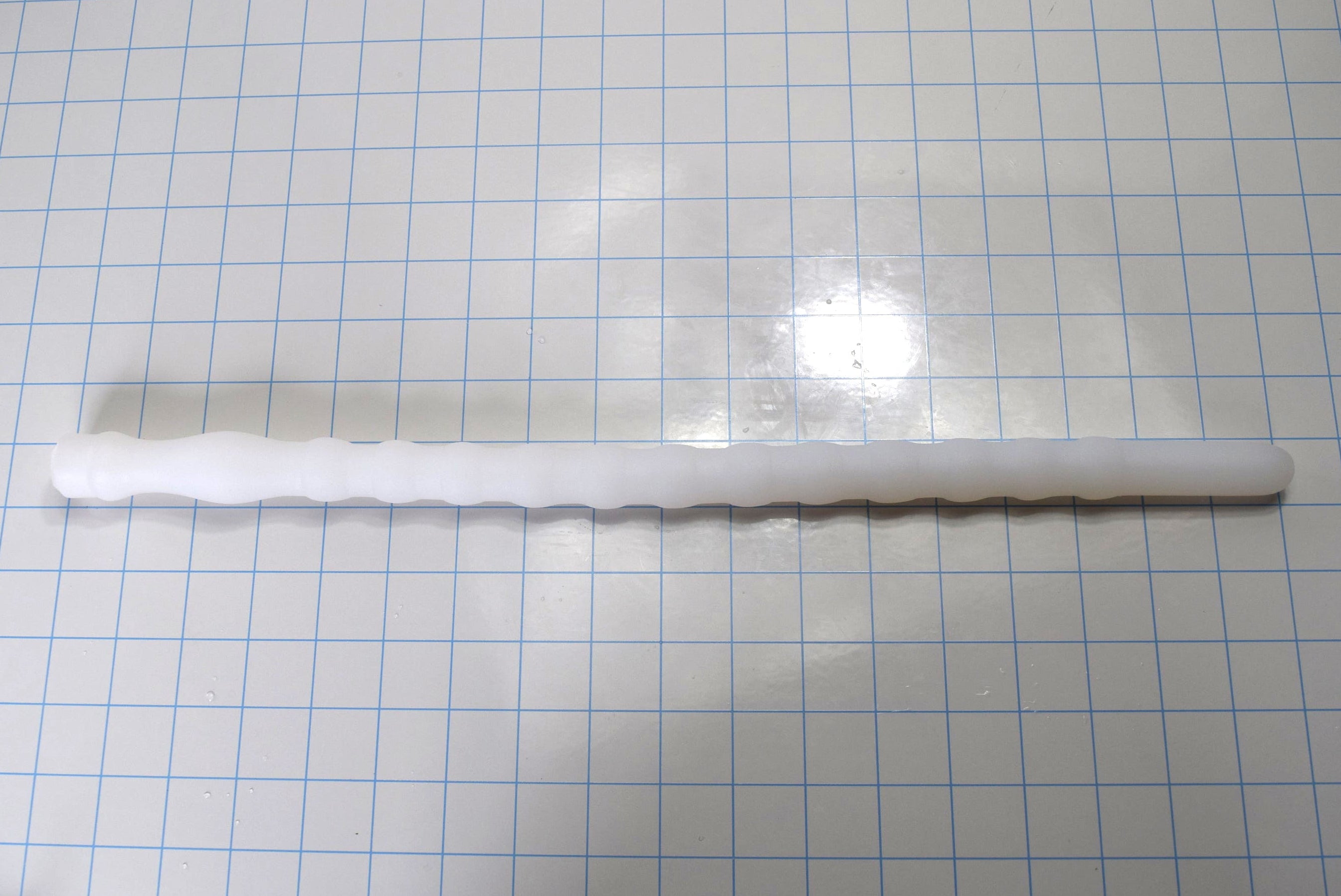 Shower Shooter 18-inch silicone enema nozzle laid flat on grid paper showing 12 expansion ribs, smooth entry tip, and retention neck.