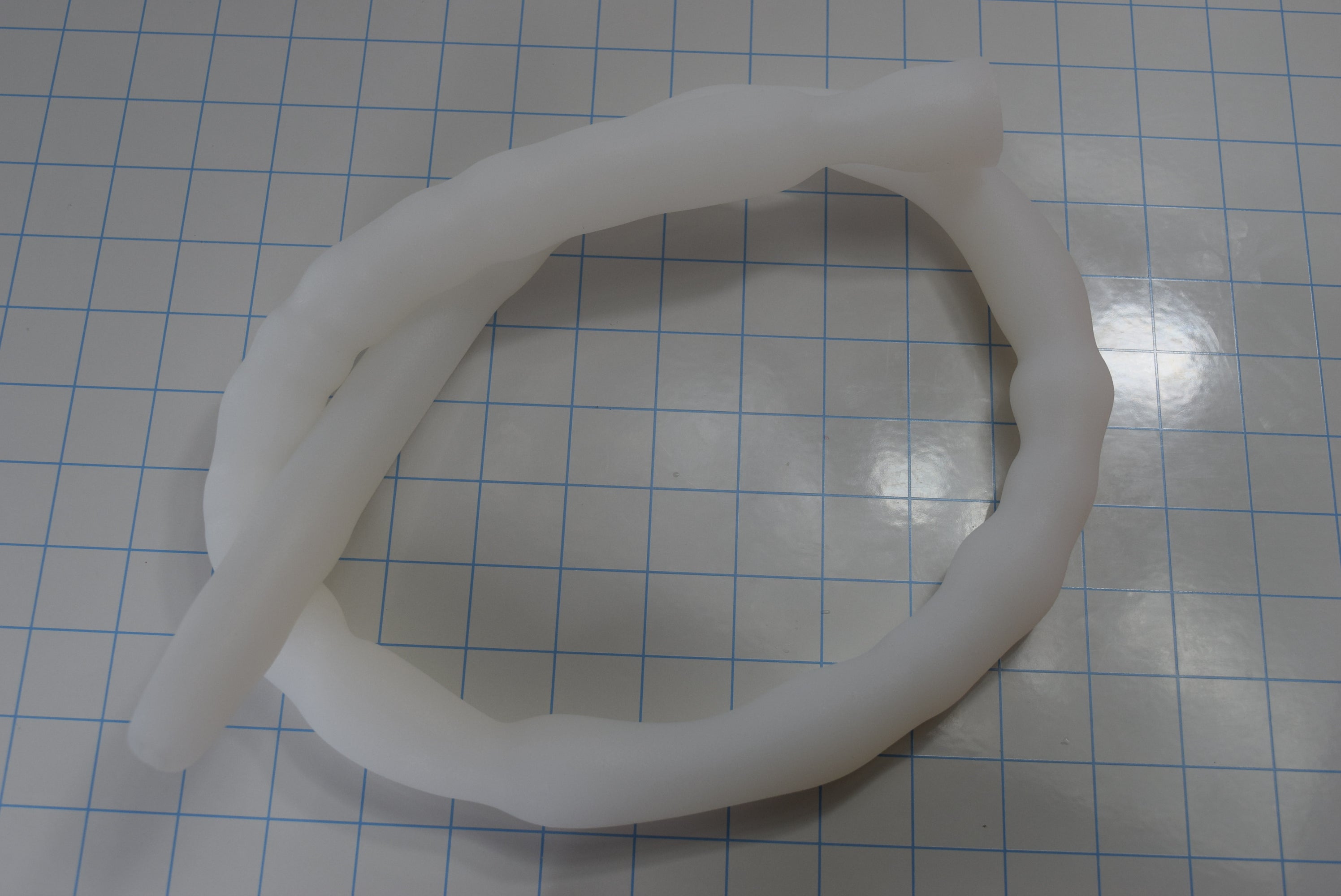 39-inch XL silicone colon tube double-looped on grid paper displaying ribbed shaft geometry and tapered entry tip.