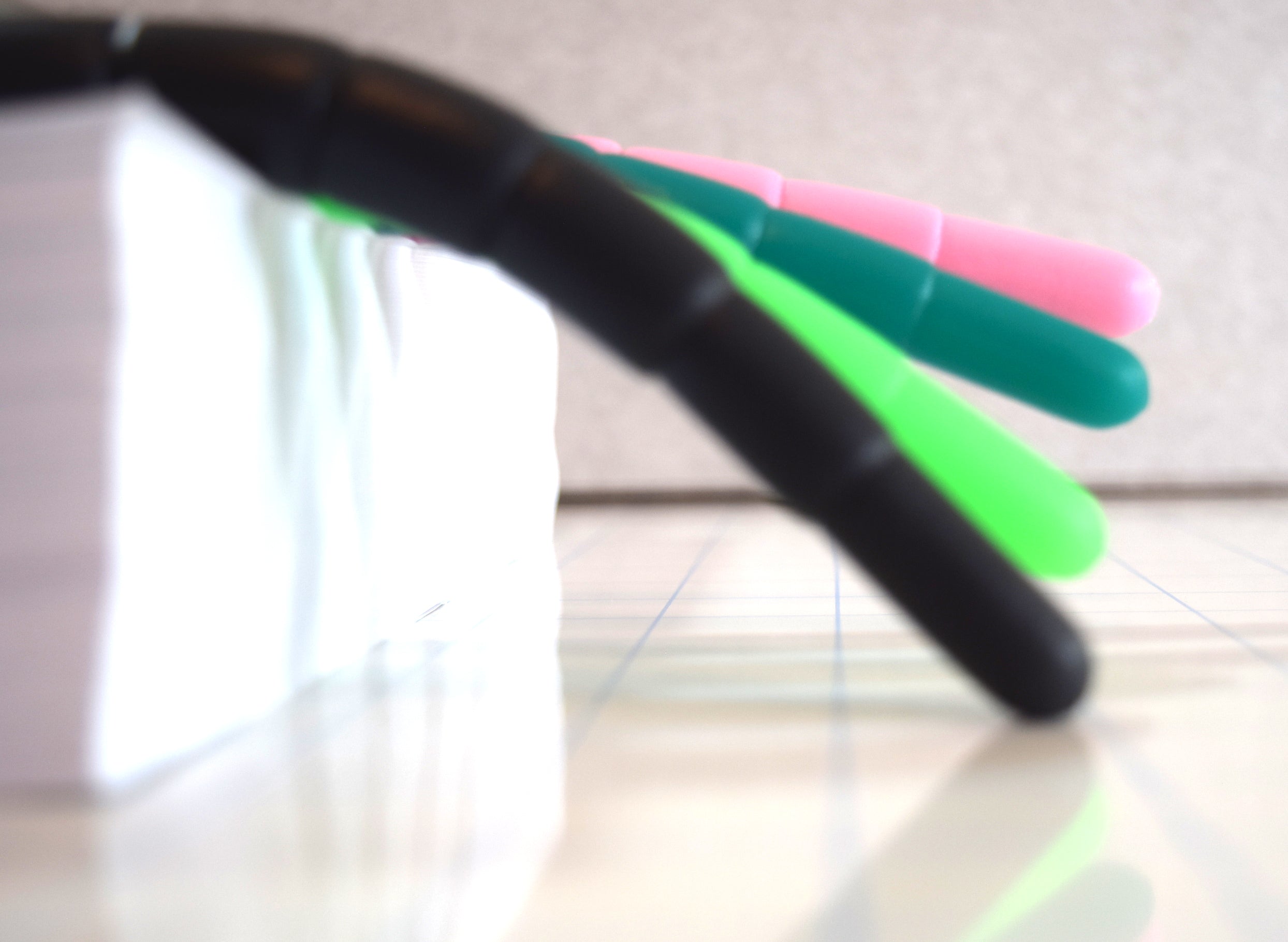 Close-up side view of four colorful silicone urethral sounds extending over a block showing varying flexibility and droop levels