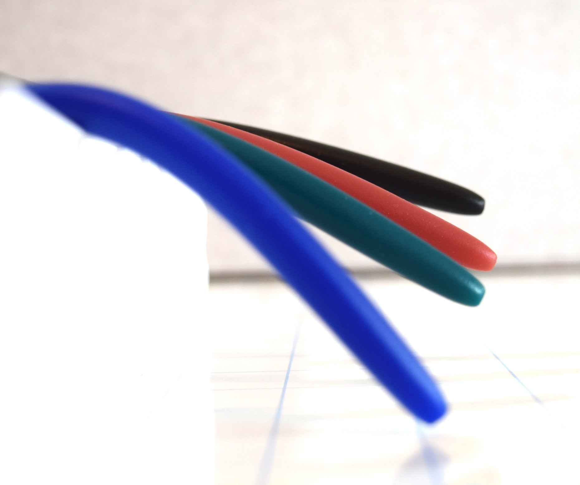 Side profile comparison of four silicone urethral sounds in different colors drooping at various angles to demonstrate firmness levels on a grid background