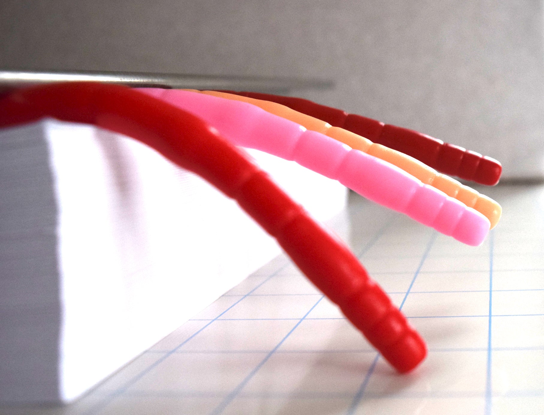 Side profile view close-up showing silicone urethral sounds extending horizontally over a grid paper surface to demonstrate firmness and droop angle