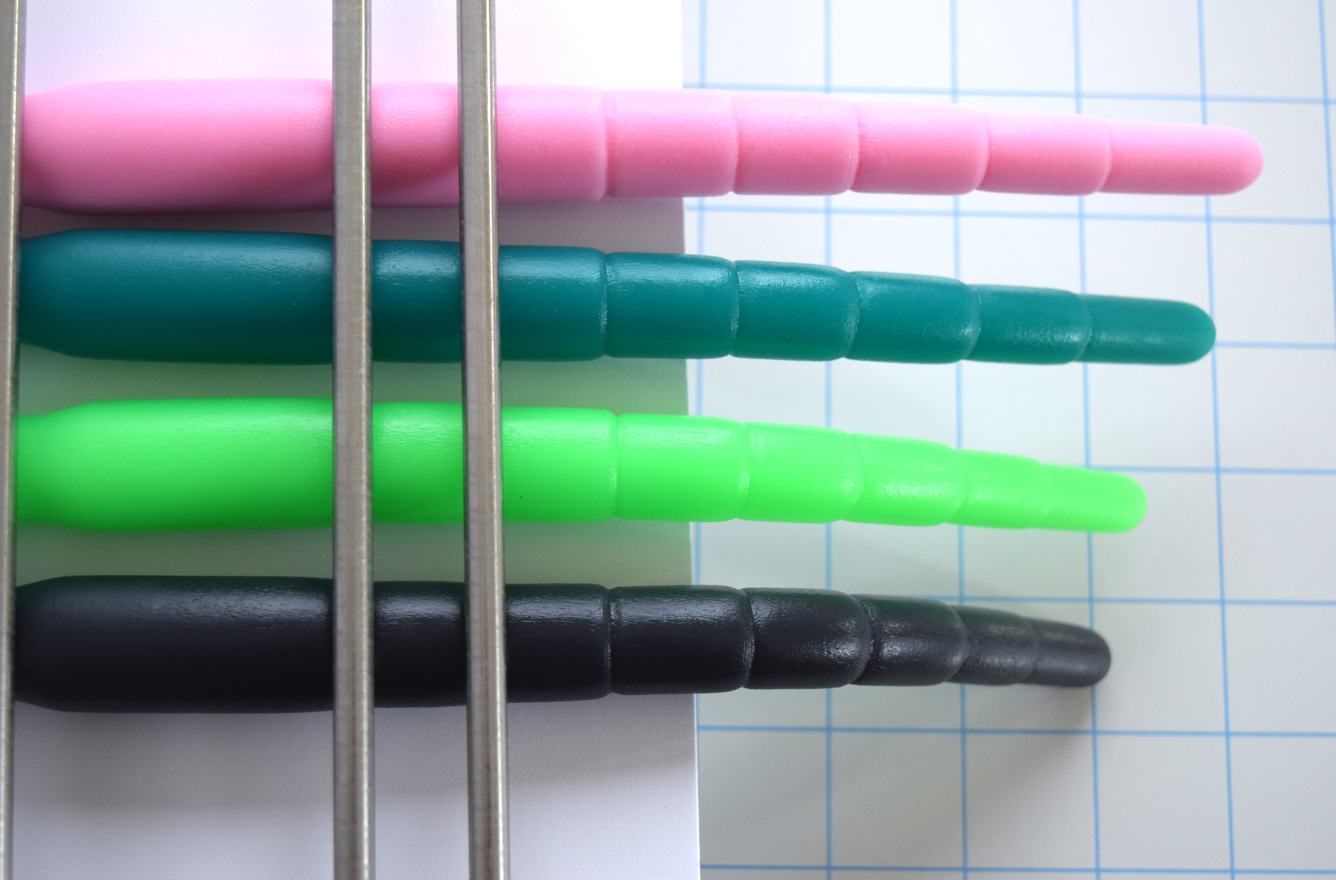Top-down view of pink, dark teal, bright green, and black segmented silicone urethral sounds held horizontally to illustrate firmness and flexibility