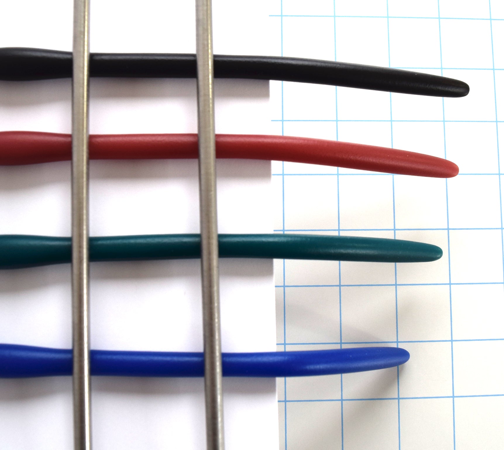 Top-down close-up view of black, red, teal, and blue silicone urethral sounds clamped side-by-side over a grid background to show material stiffness and bend