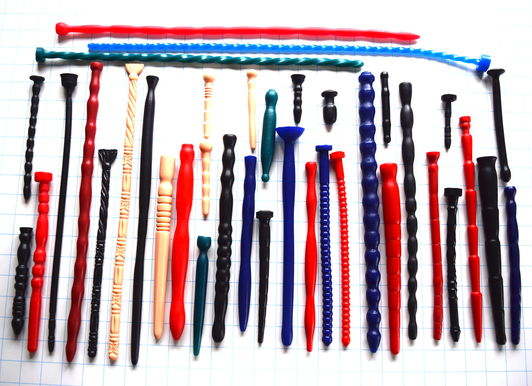 An assortment of silicone urethral sounds in various textures, sizes, and colors arranged on a blue grid background.