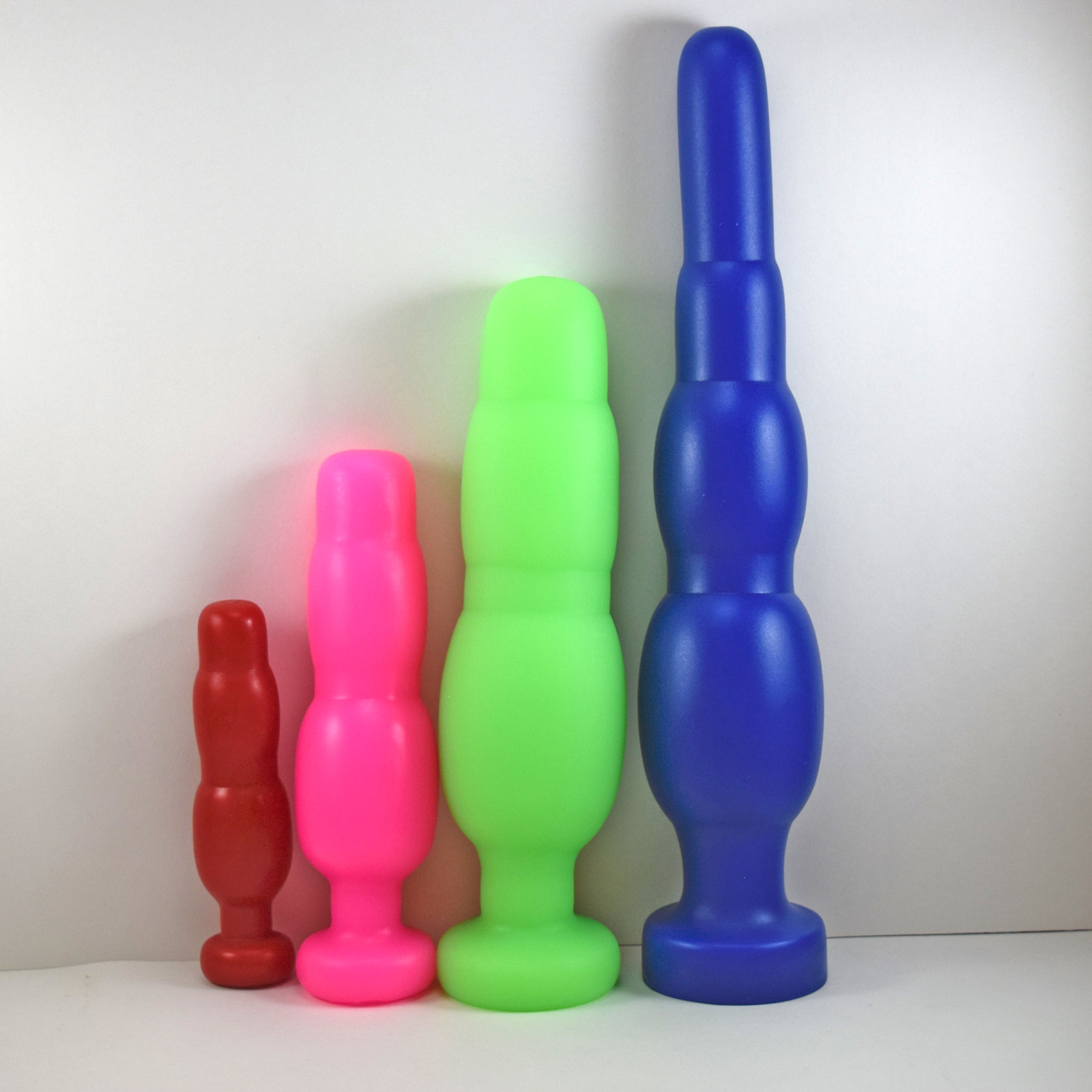 Comparison lineup of four SNC silicone retention nozzles lined up vertically from smallest to largest (SNC MINI in red, SNC MED in pink, SNC MAX in green, and SNC MAX EXT in blue) on a white background.