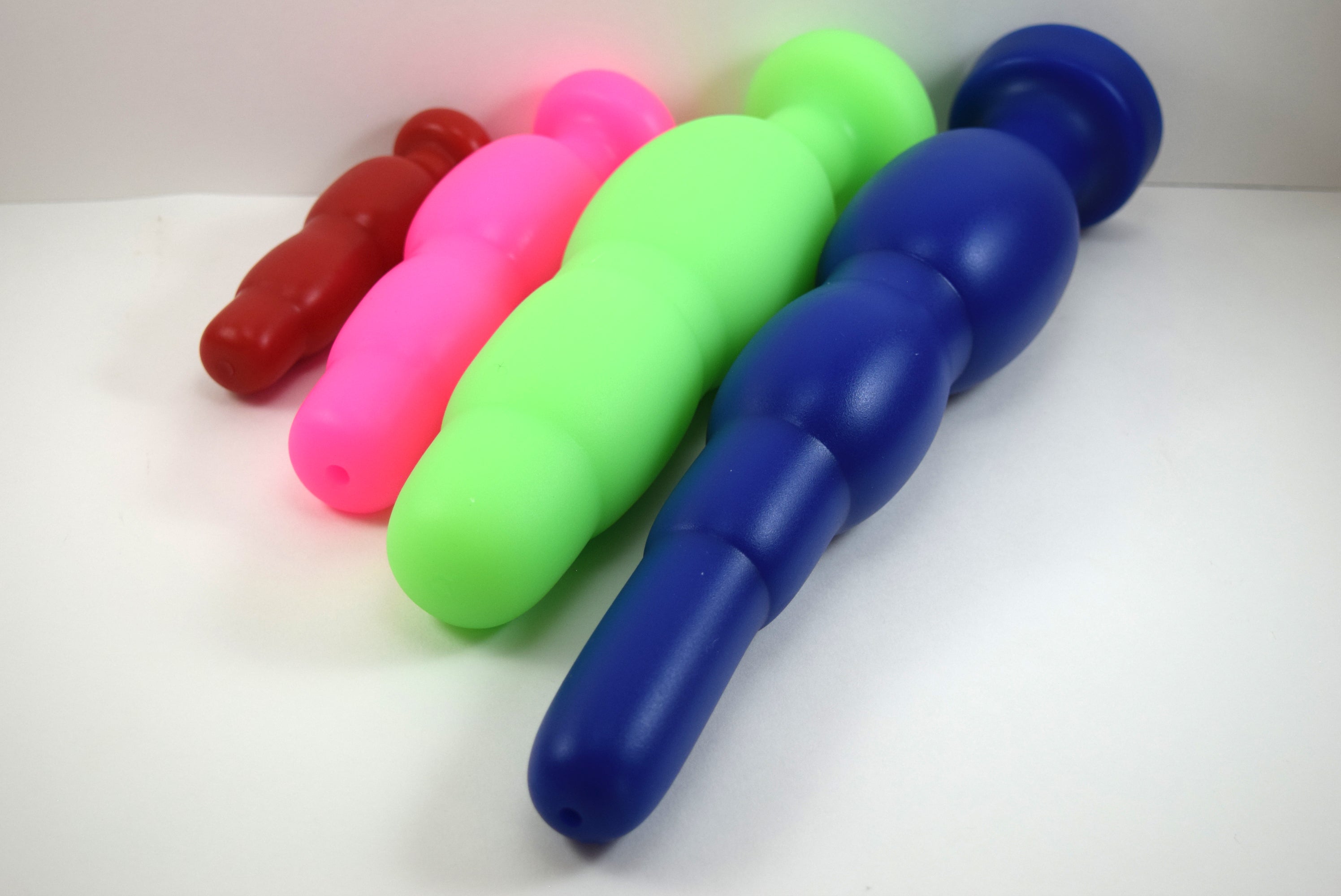 Perspective view of four SNC silicone retention nozzles lined up diagonally from smallest to largest (red SNC MINI, pink SNC MED, green SNC MAX, and blue SNC MAX EXT) on a white background.