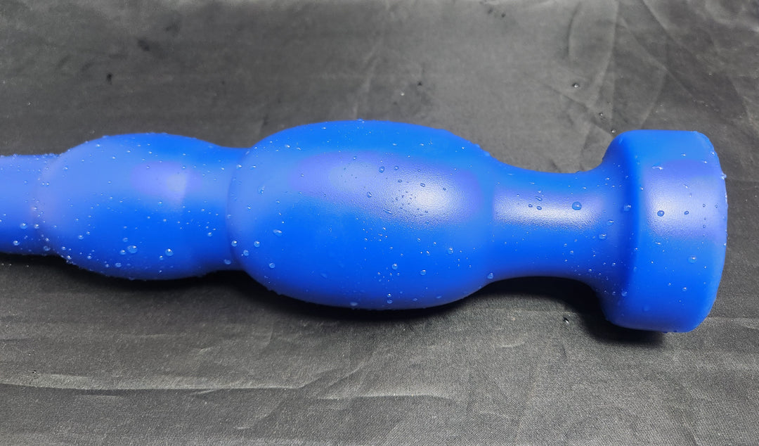 Blue silicone SNC MAX EXT retention nozzle resting on a grey background, featuring an extended 1.5-inch nose tip, multi-tiered 3.0-inch expansion bulbs, and a safety base flange.