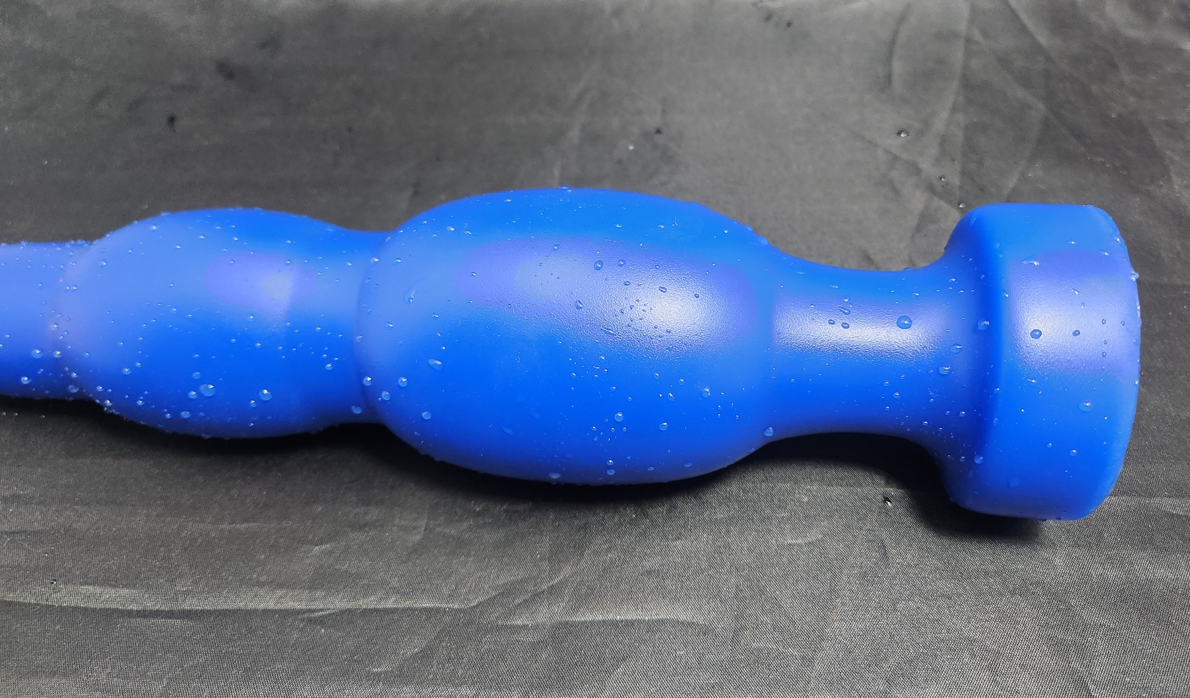 Blue silicone SNC MAX EXT retention nozzle resting on a grey background, featuring an extended 1.5-inch nose tip, multi-tiered 3.0-inch expansion bulbs, and a safety base flange.