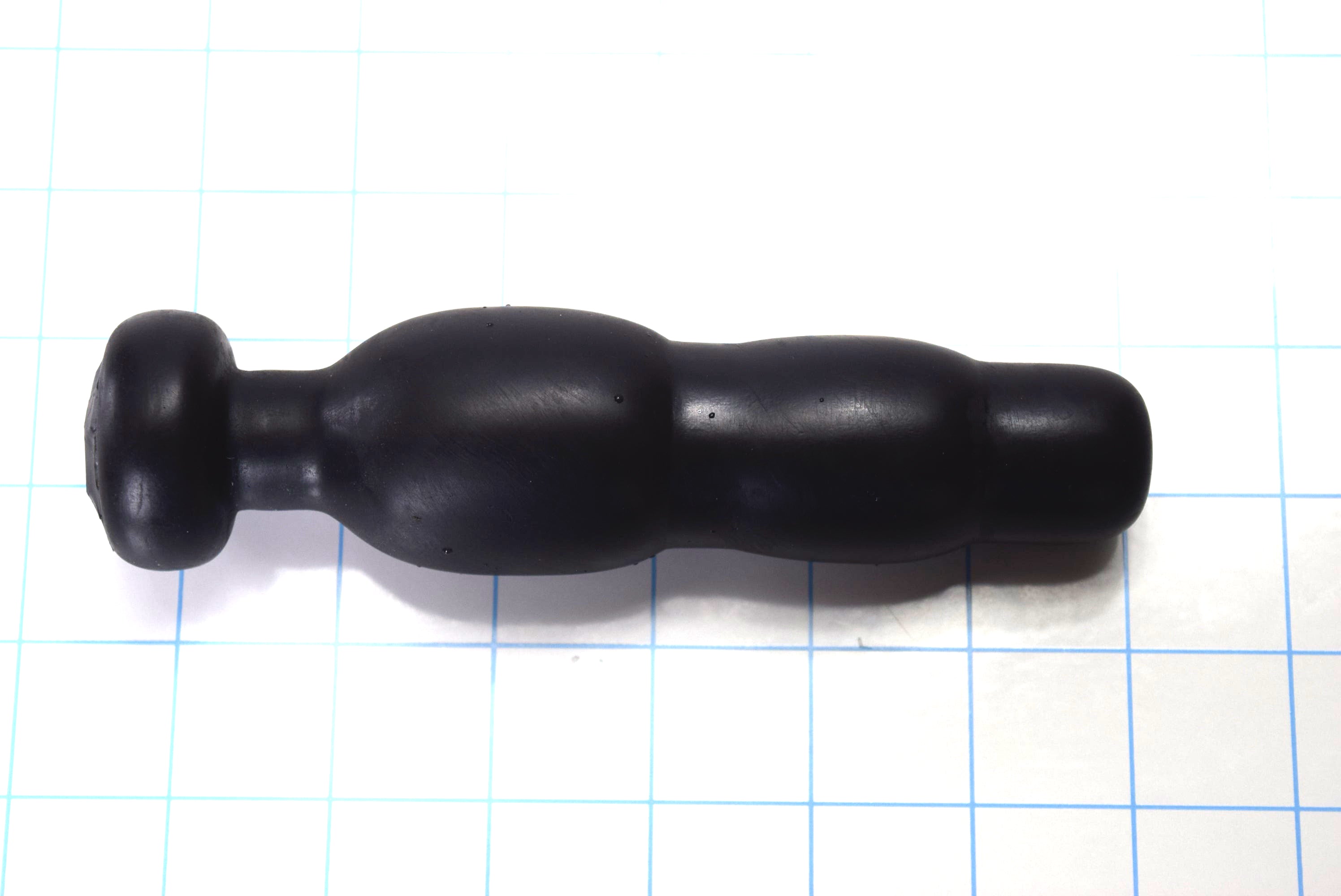 Black silicone SNC MINI retention nozzle with a compact triple-bulb design and safety flange resting on a blue grid background.