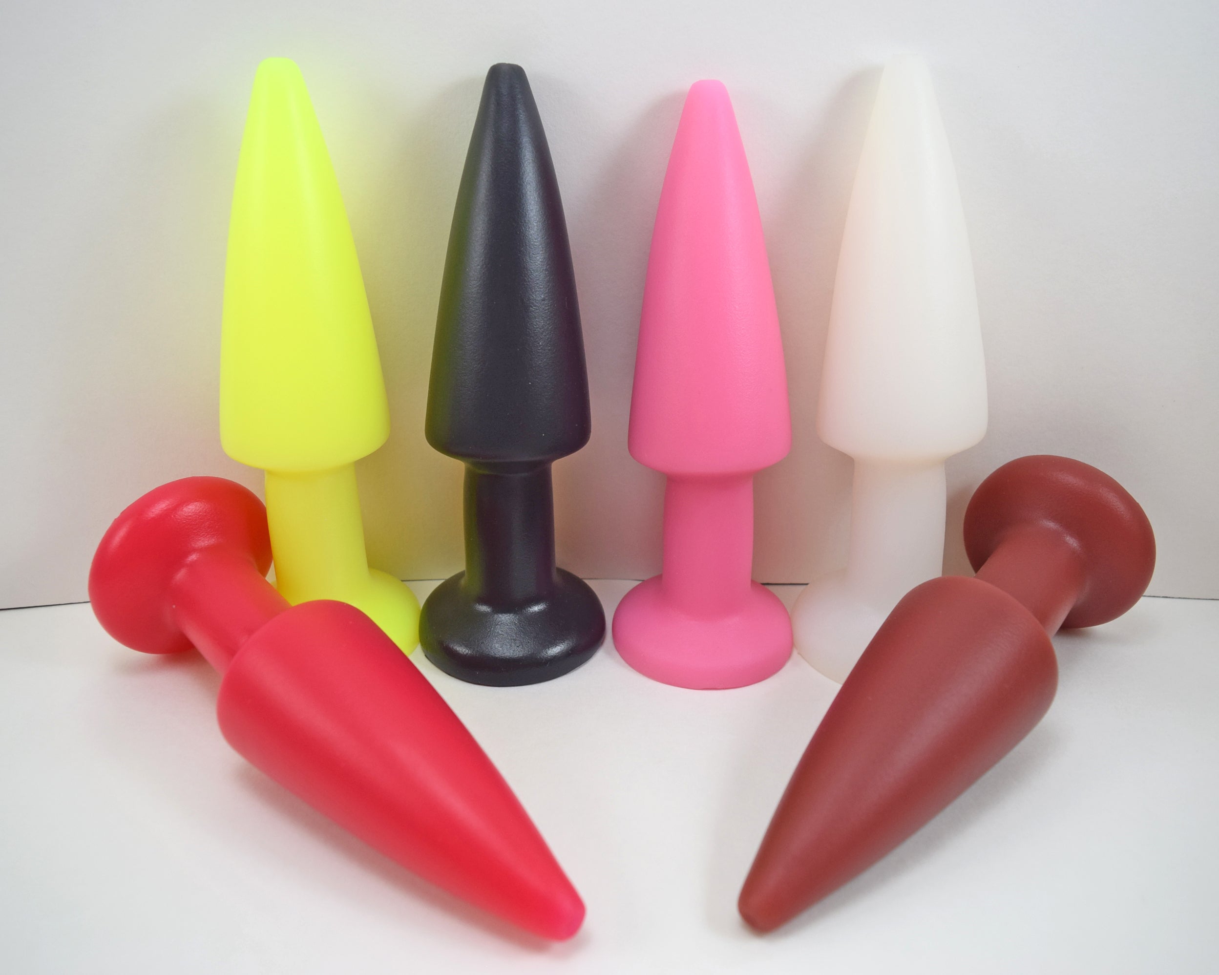Six SPD 2.0-inch silicone enema nozzles in yellow, black, pink, translucent white, red, and brown showing tapered tips and retention valleys.