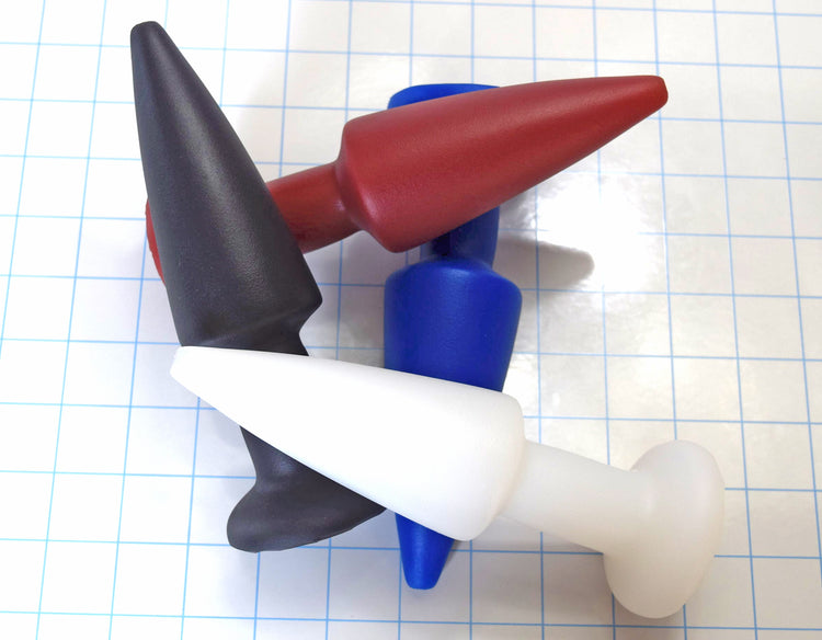 A stack of four colorful silicone retention enema nozzles arranged over each other on a blue grid background.