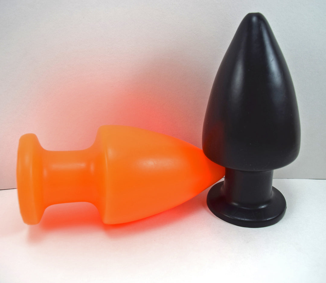 Orange silicone retention enema nozzle lying horizontally beside an upright black nozzle on a white background.