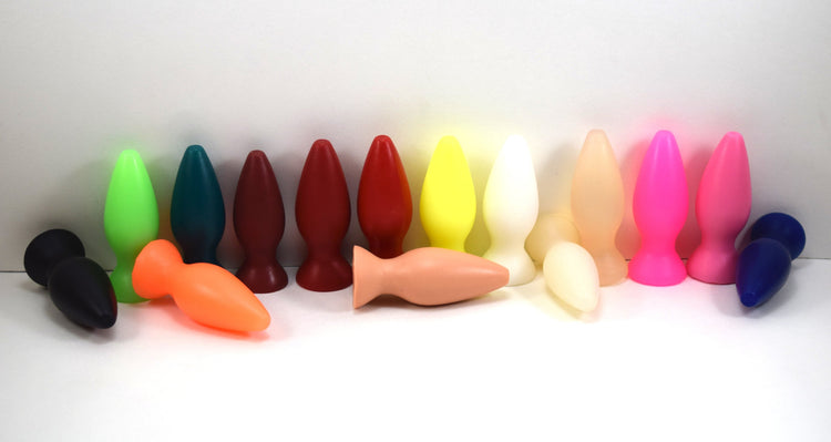 A row of small silicone retention plugs in multiple bright colors standing and lying on a white background.