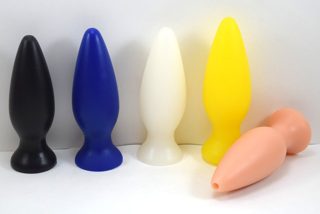 A row of colorful silicone retention enema nozzles shown standing upright and lying down on a white surface.