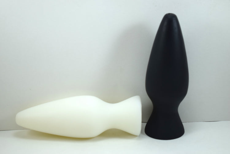 White silicone retention plug lying horizontally alongside an upright black silicone plug on a white surface.
