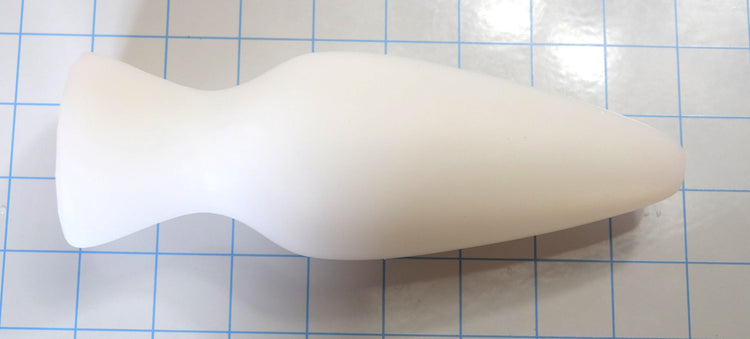 White silicone retention plug lying horizontally on a blue grid background.