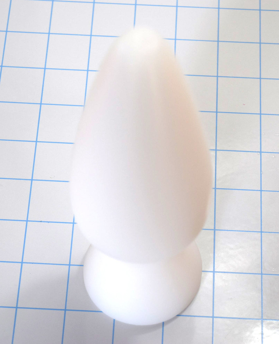 White silicone retention plug standing upright on a blue grid background.