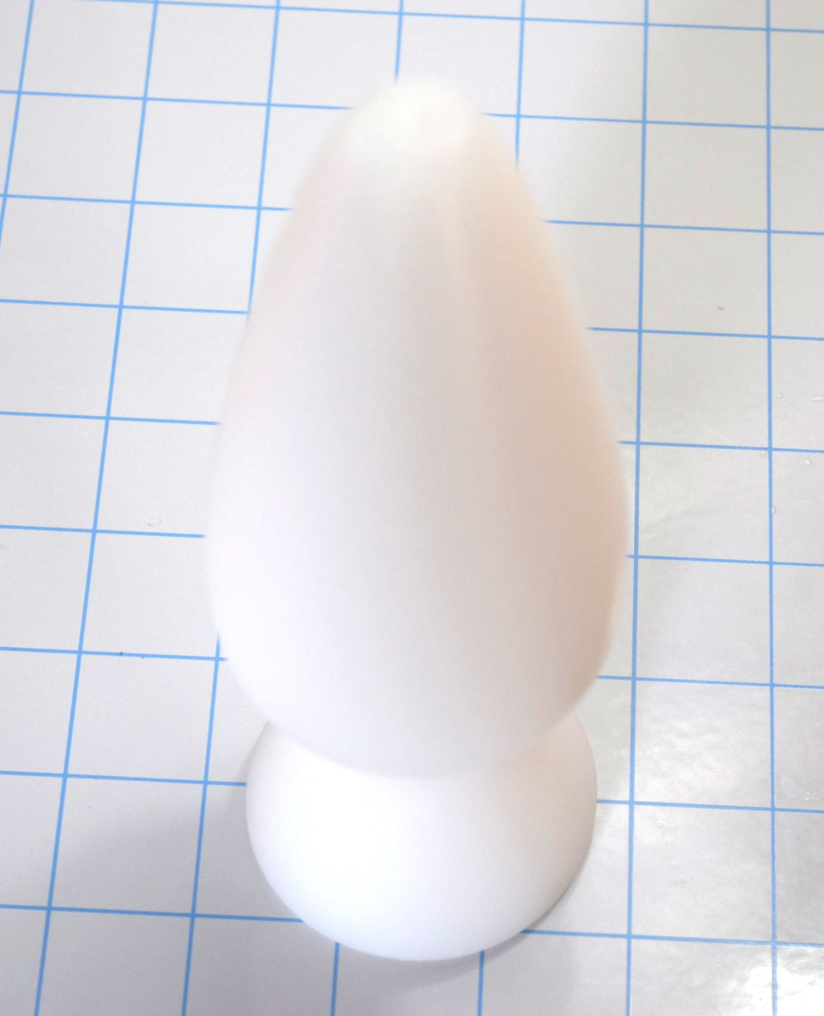 White silicone retention plug standing upright on a blue grid background.