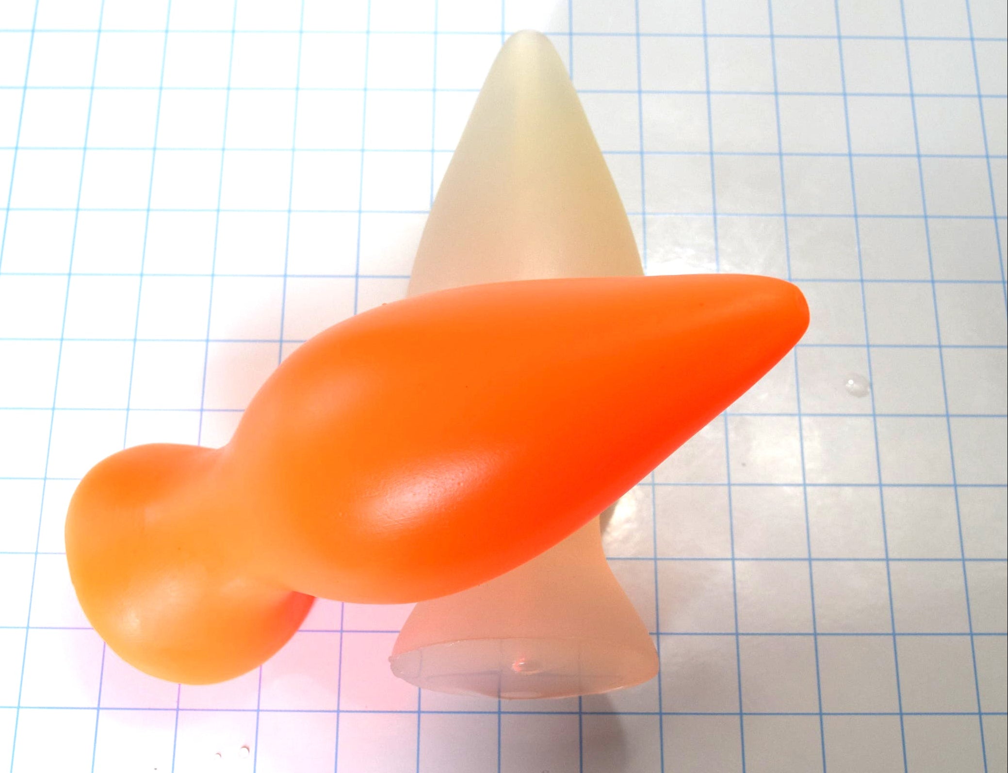 Orange and clear silicone retention plugs crossed over each other on a blue grid background.