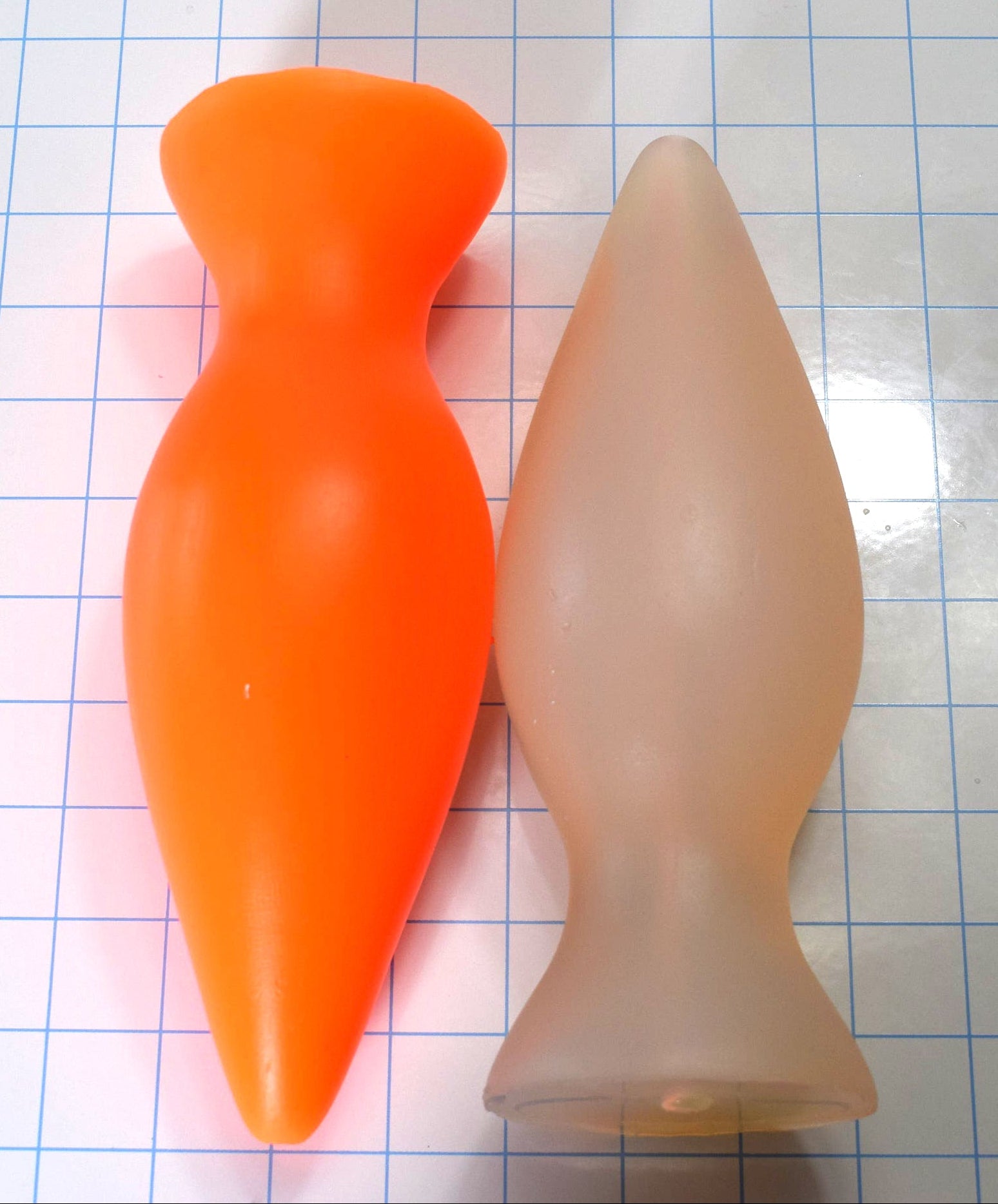 Fluorescent orange and flesh-toned silicone retention plugs standing side-by-side vertically on a blue grid background.