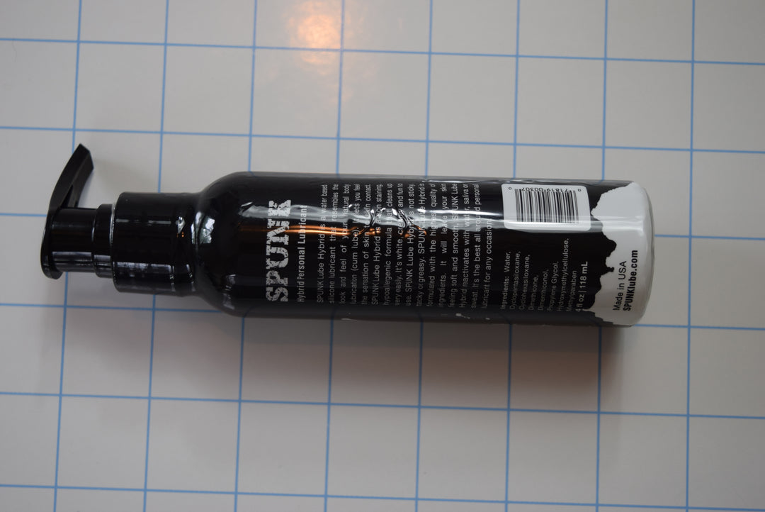 Back view of the 4oz black pump bottle of SPUNK Hybrid personal lubricant showing ingredients and label details on a blue grid background.