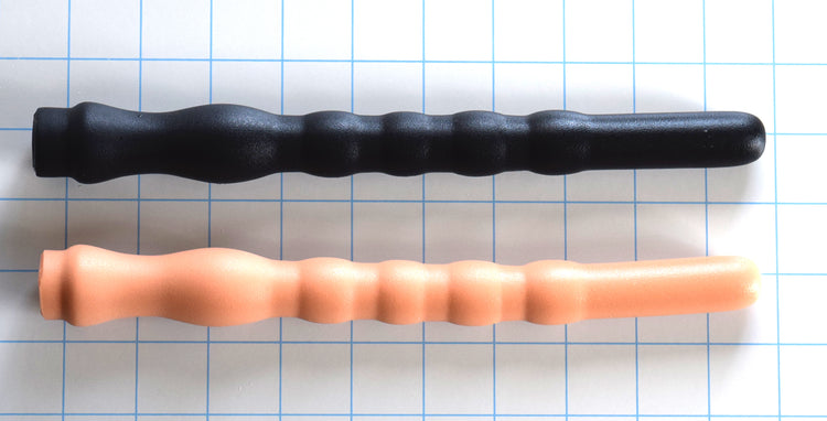 Two Shower Shooter 9-inch silicone utility nozzles in black and flesh tones laid horizontally on a blue grid background, highlighting the 0.75-inch smooth tip, four 0.85-inch expansion ribs, and 0.75-inch retention valley.