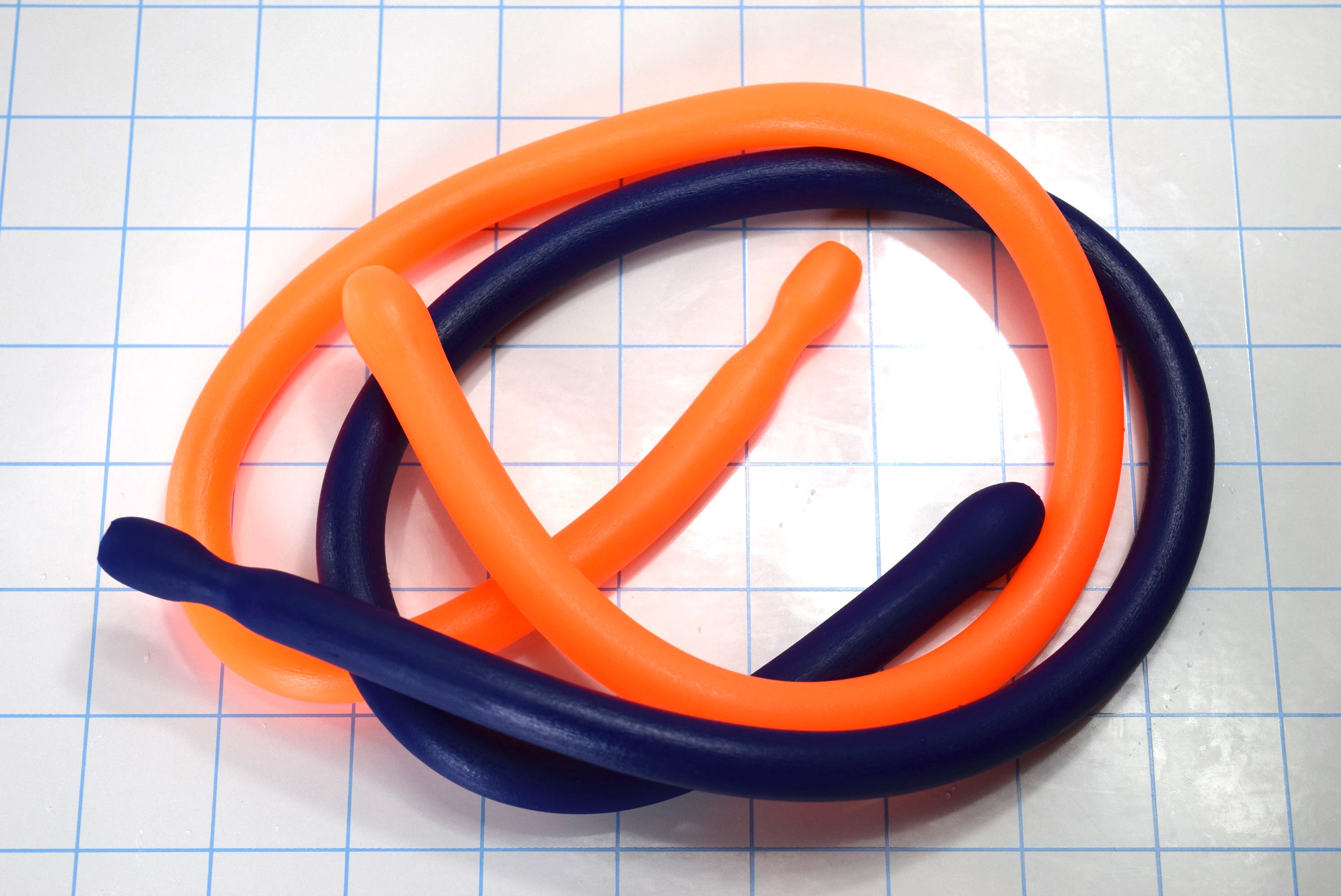Alternative view of orange and blue flexible SSND_24_BT silicone sounds looped in an oval shape on a blue grid background, highlighting the 14mm egg-shaped tips and 12mm shafts.