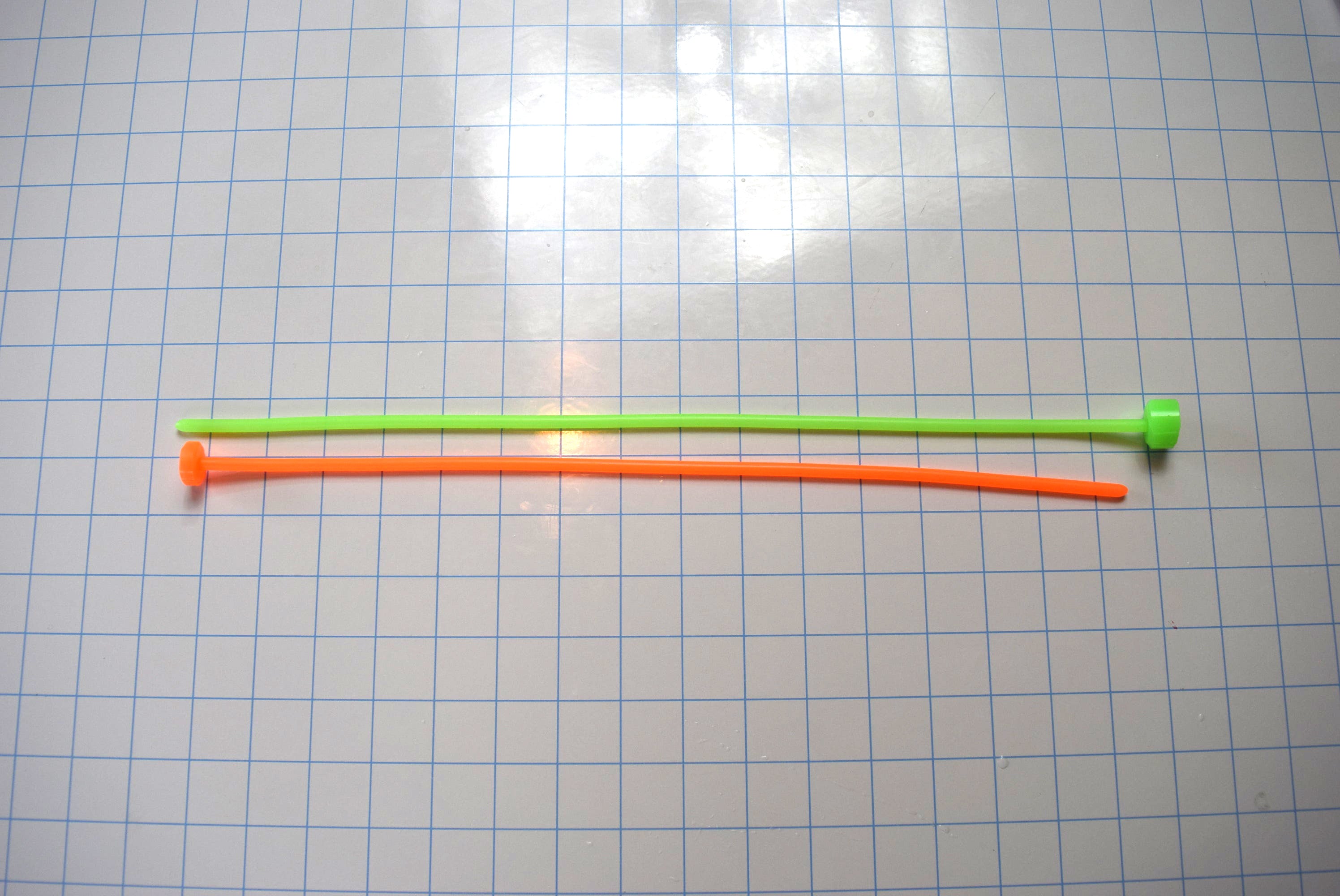 SSND-5.5mm silicone urethral sounds in fluorescent green and fluorescent orange featuring 5.5mm diameters (16 French), smooth rounded tips, solid core constructions, and 15-inch insertable lengths displayed side-by-side on a grid background.