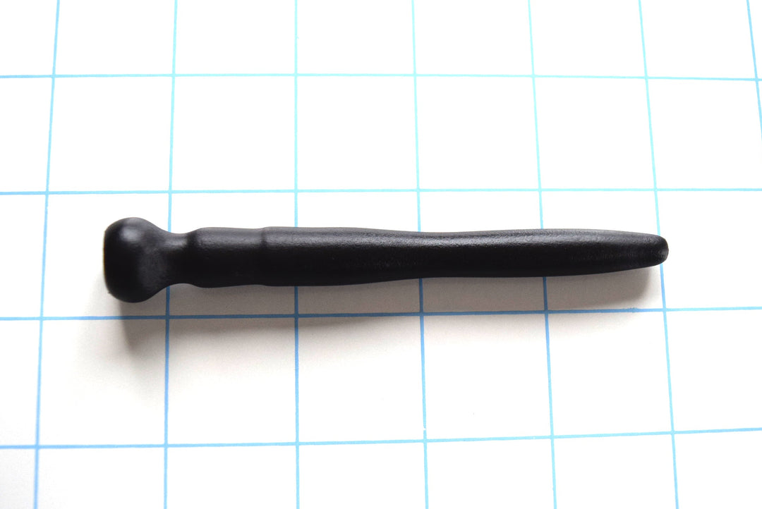 Black silicone urethral sound with a tapered tip and flanged base resting on a blue grid background.
