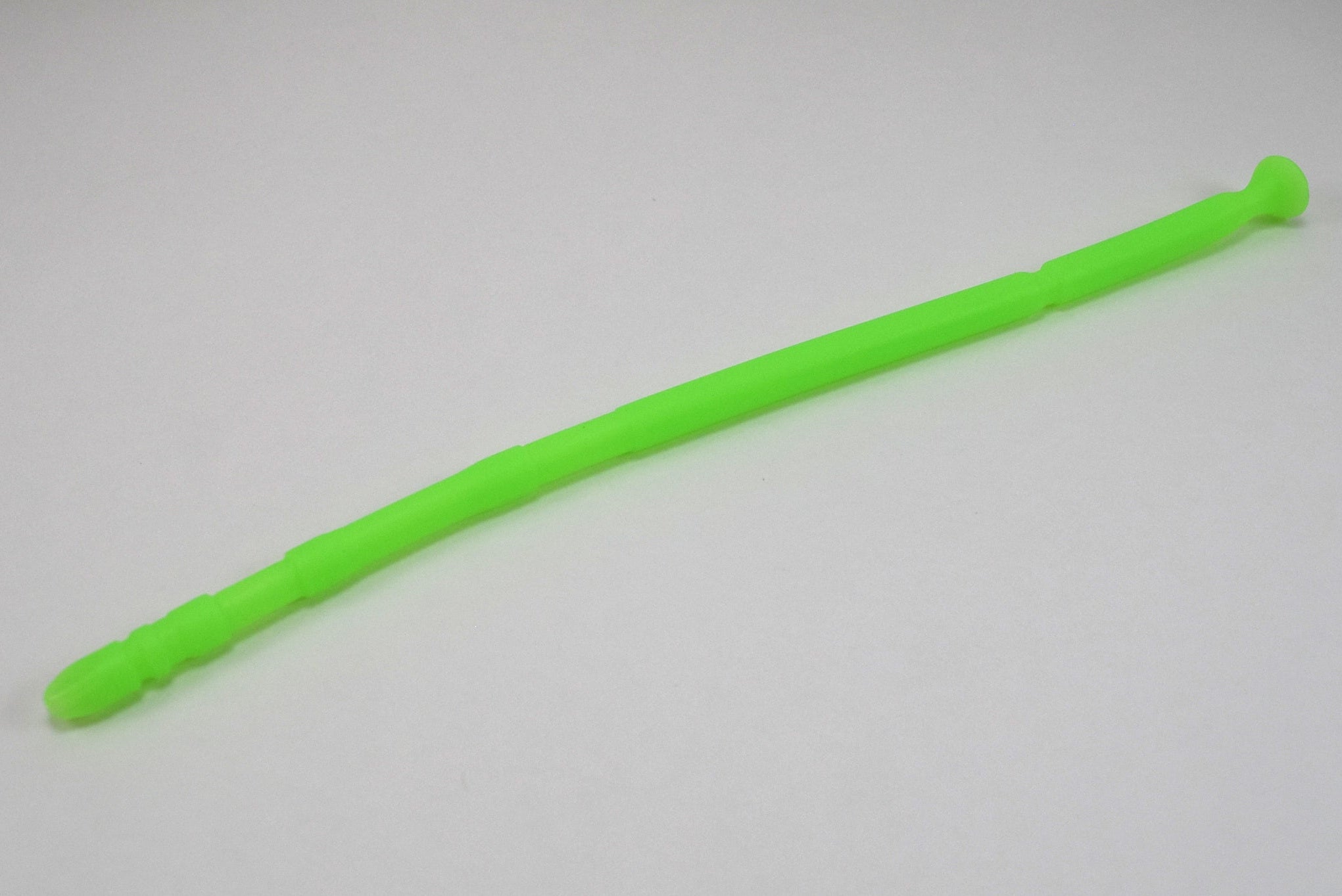 A fluorescent green 13-inch contoured silicone sound with a multi-faceted tip lying diagonally on a plain white surface.