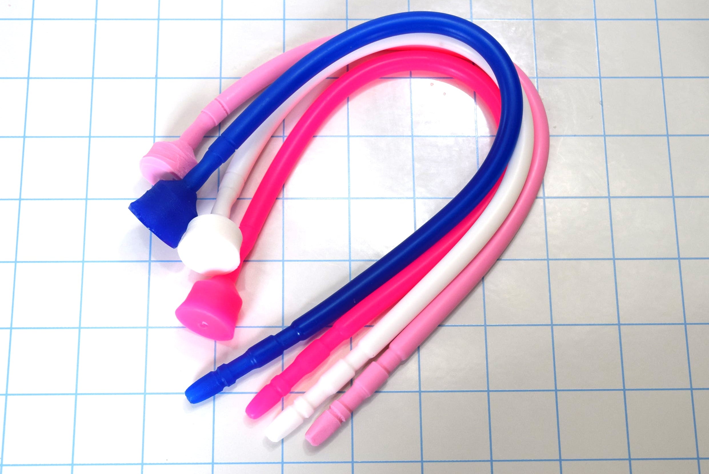 Four 13-inch contoured silicone sounds in blue, white, and pink shades bent in a U-shape on a blue grid mat.