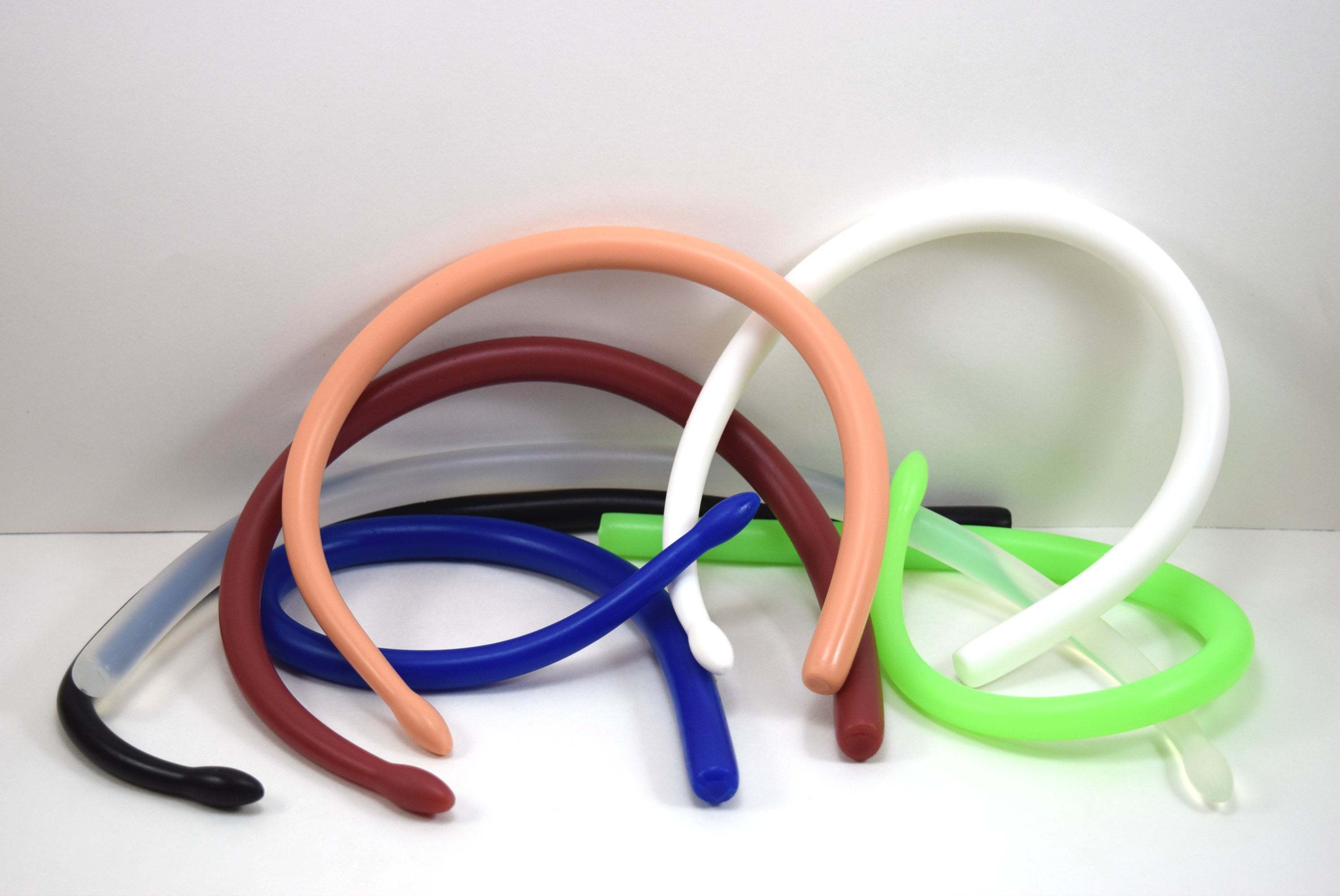 Multiple SSND-DRUMSTICK silicone urethral sounds with contoured tips bent into flexible curves, shown in various colors including peach, white, blue, red, green, and black.