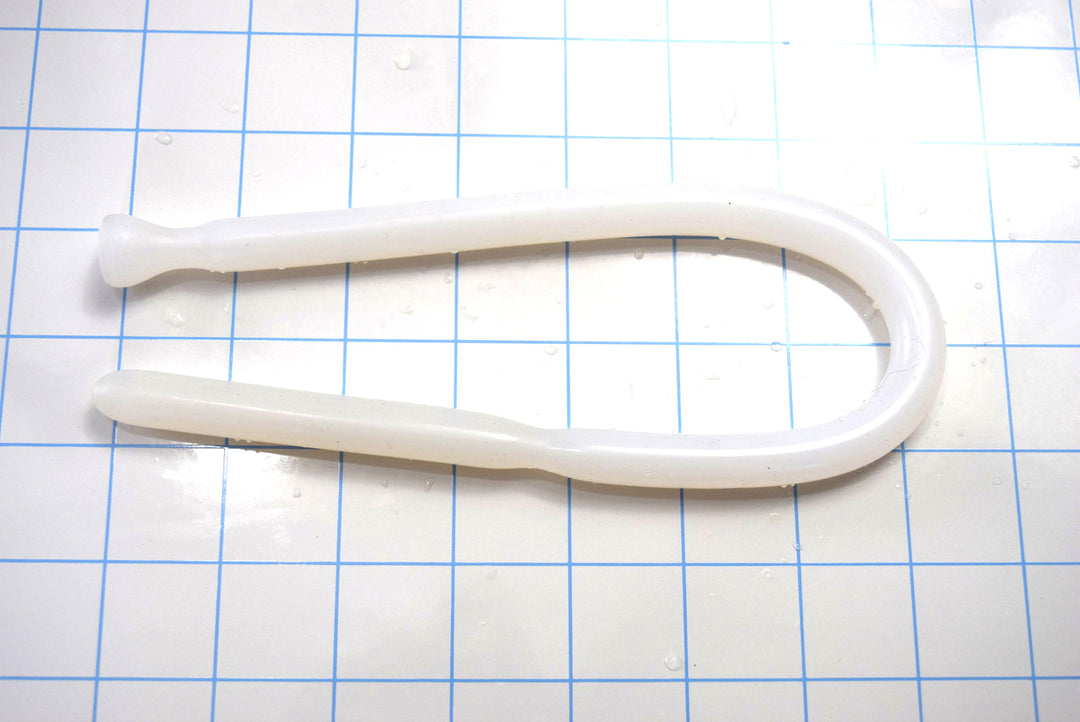 Translucent white SSND-DS 9-12 flexible silicone sound bent in a U-shape on a blue grid mat, displaying its grooved tip and flanged safety base.